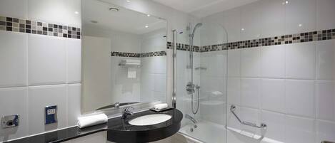 A modern bathroom with a black sink, white tiles, a glass-enclosed shower, and a mirror above the sink.