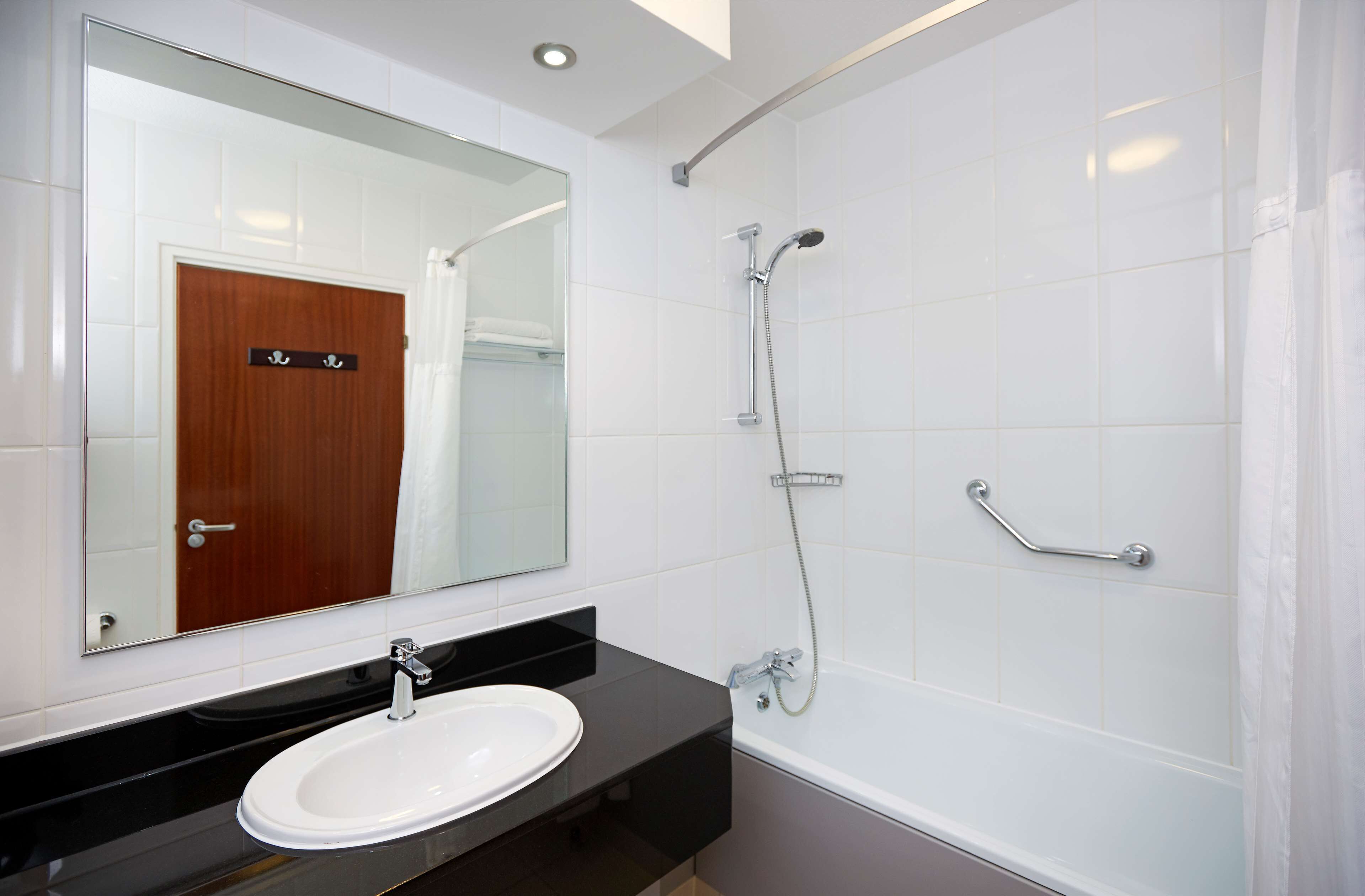 A modern bathroom with a white sink, a large mirror, and a shower with grab bars.