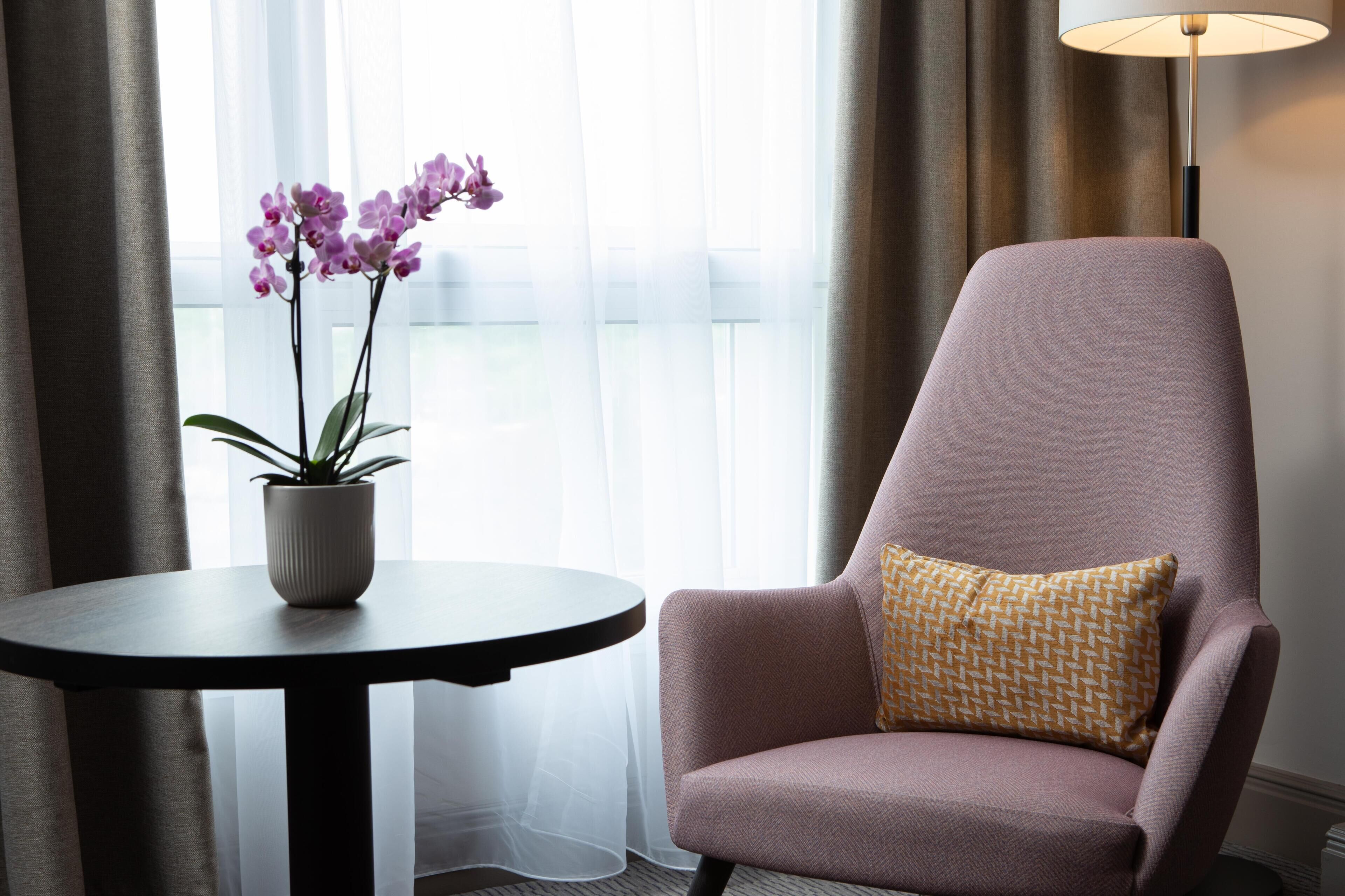 A room with a chair, a table with a potted plant, and a lamp.