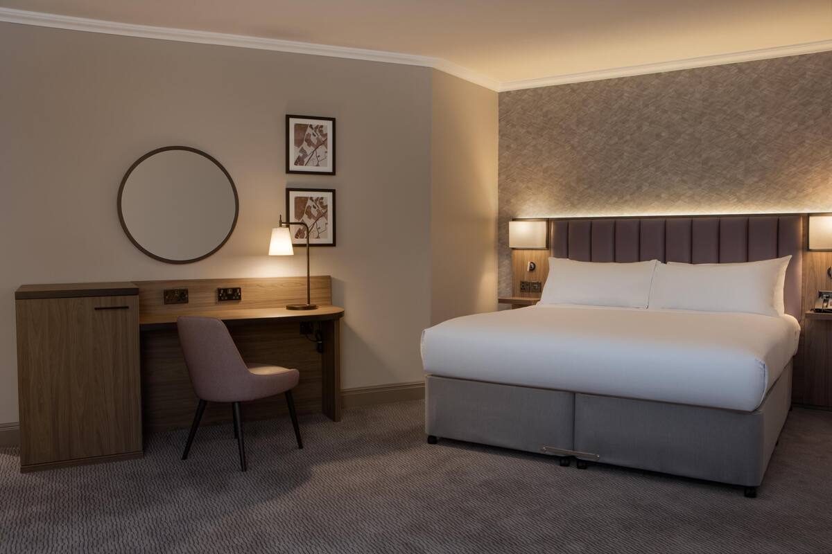Een hotelkamer met een bed, bureau, stoel en twee wandlampen.