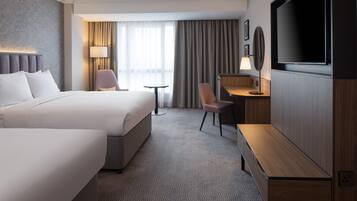 A hotel room with a large bed, a desk, a chair, a TV, and a window with curtains.