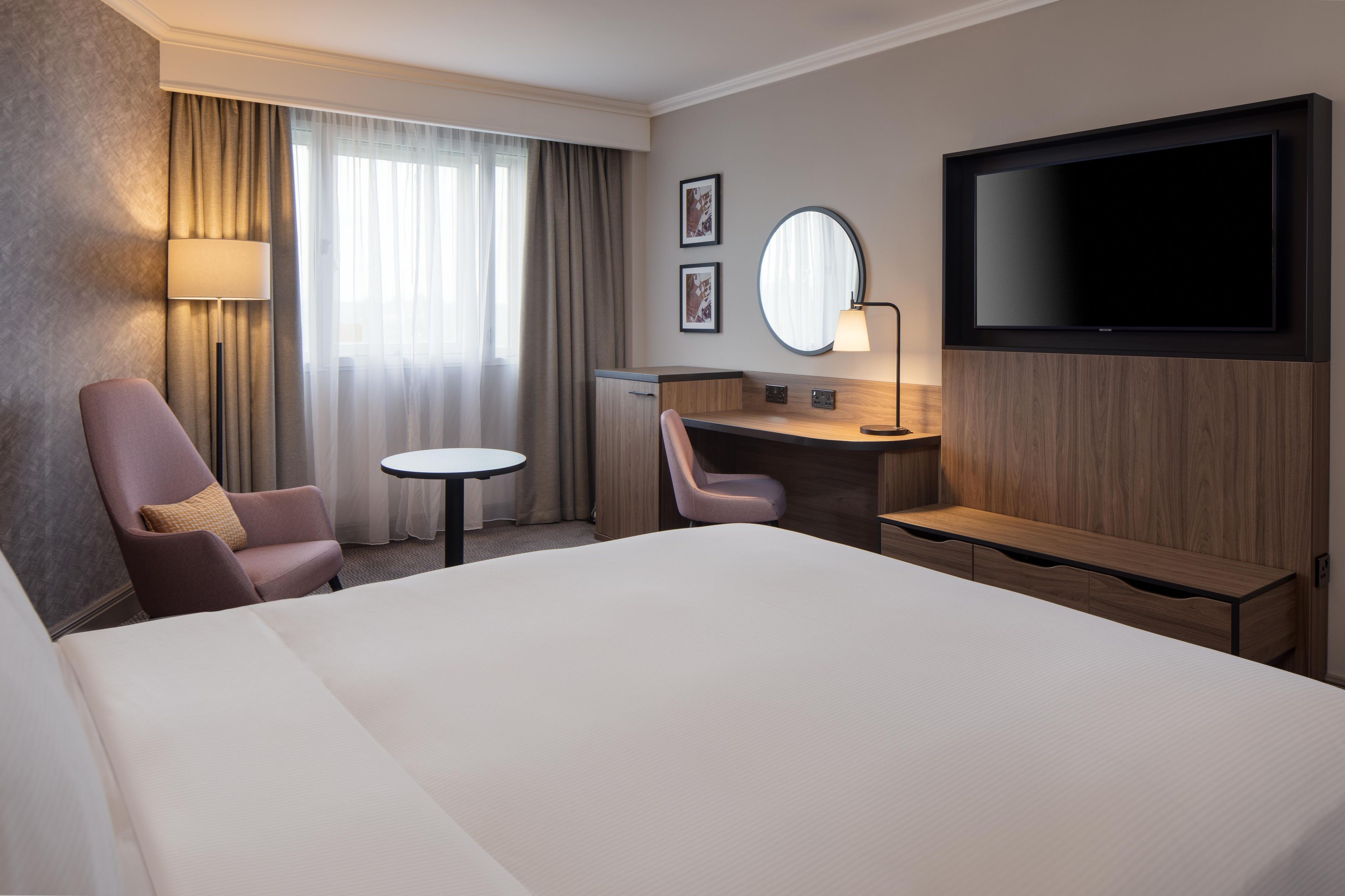 A hotel room with a large bed, a desk with a chair, a television, and a window with curtains.