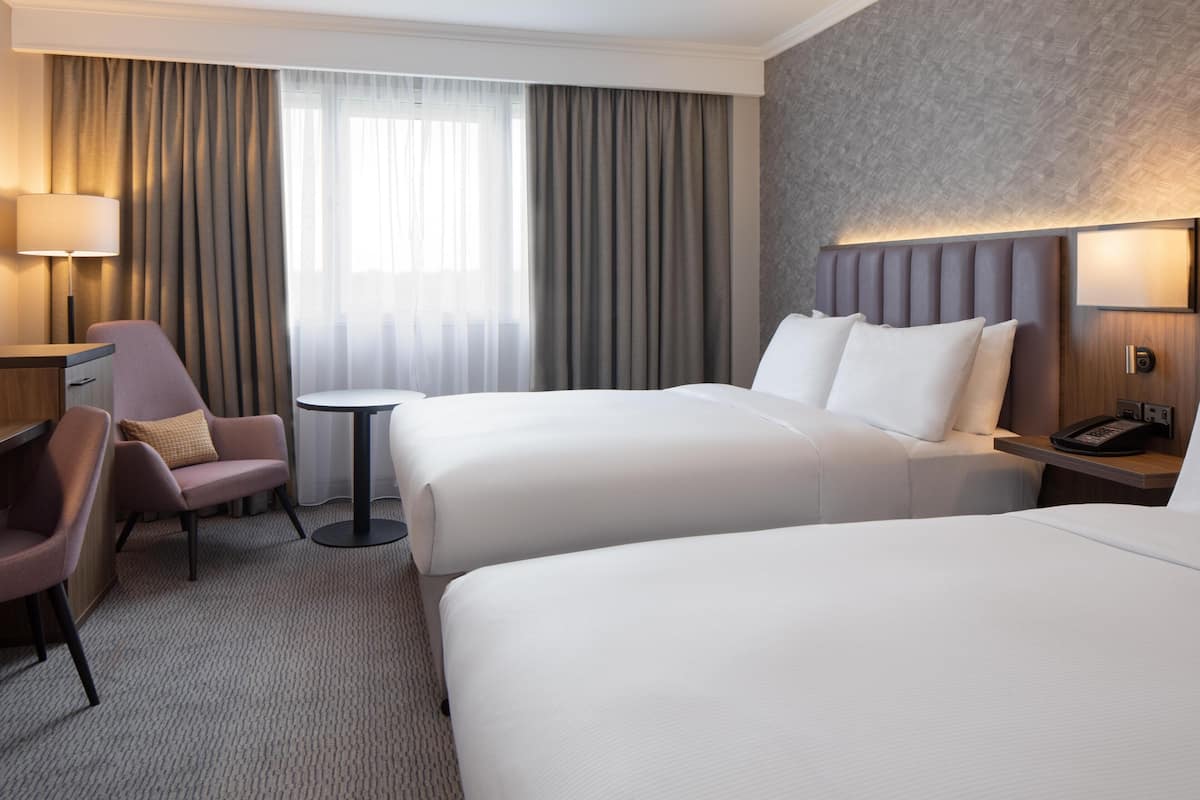 Een hotelkamer met twee bedden, een bureau, een stoel, een klein tafeltje en een lamp.