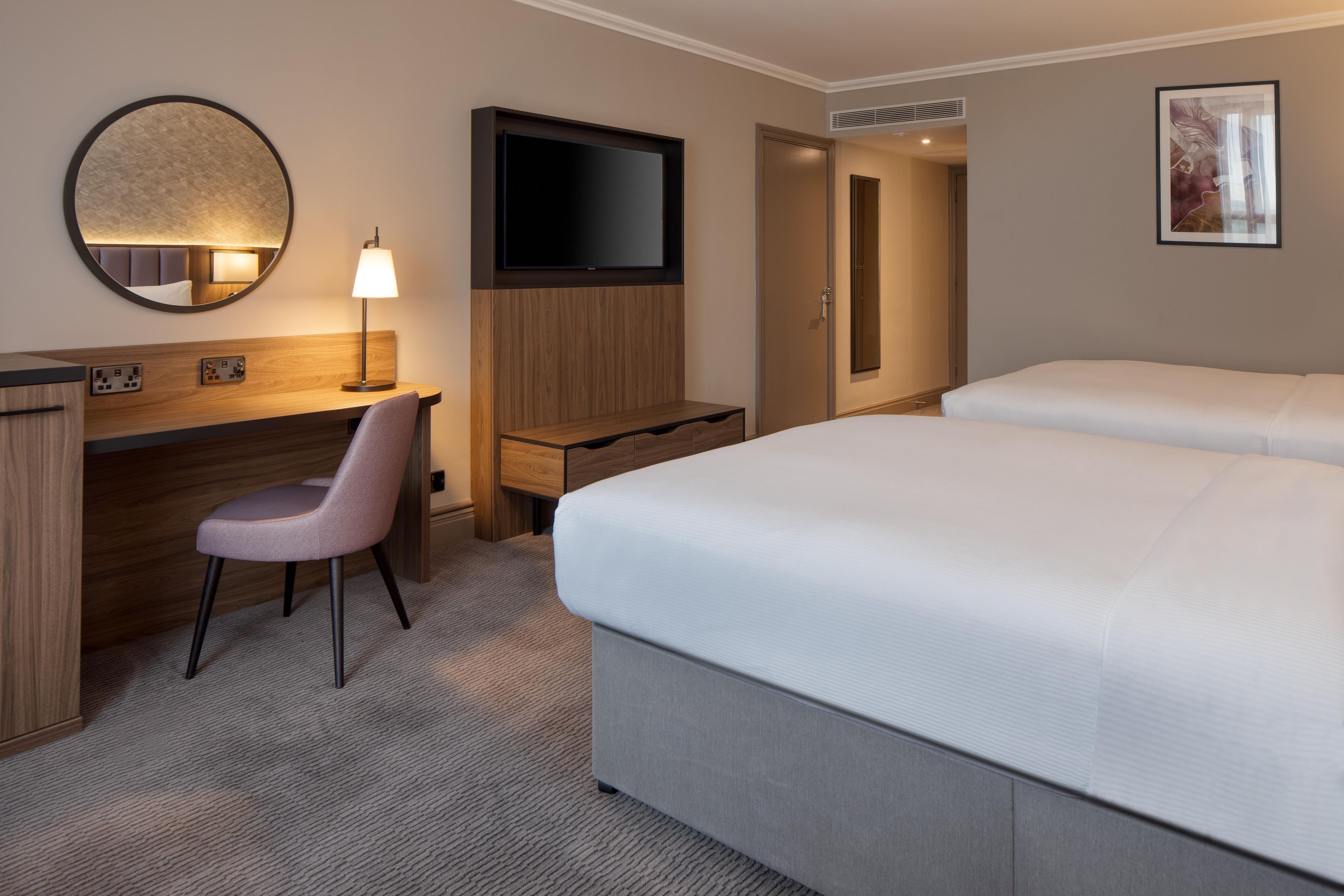 A hotel room with a bed, a desk, a chair, a TV, and a mirror.