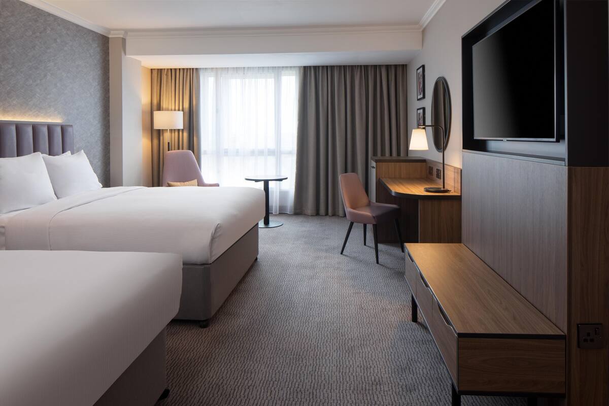 Een hotelkamer met een groot bed, een bureau, een stoel, een televisie en een raam met gordijnen.