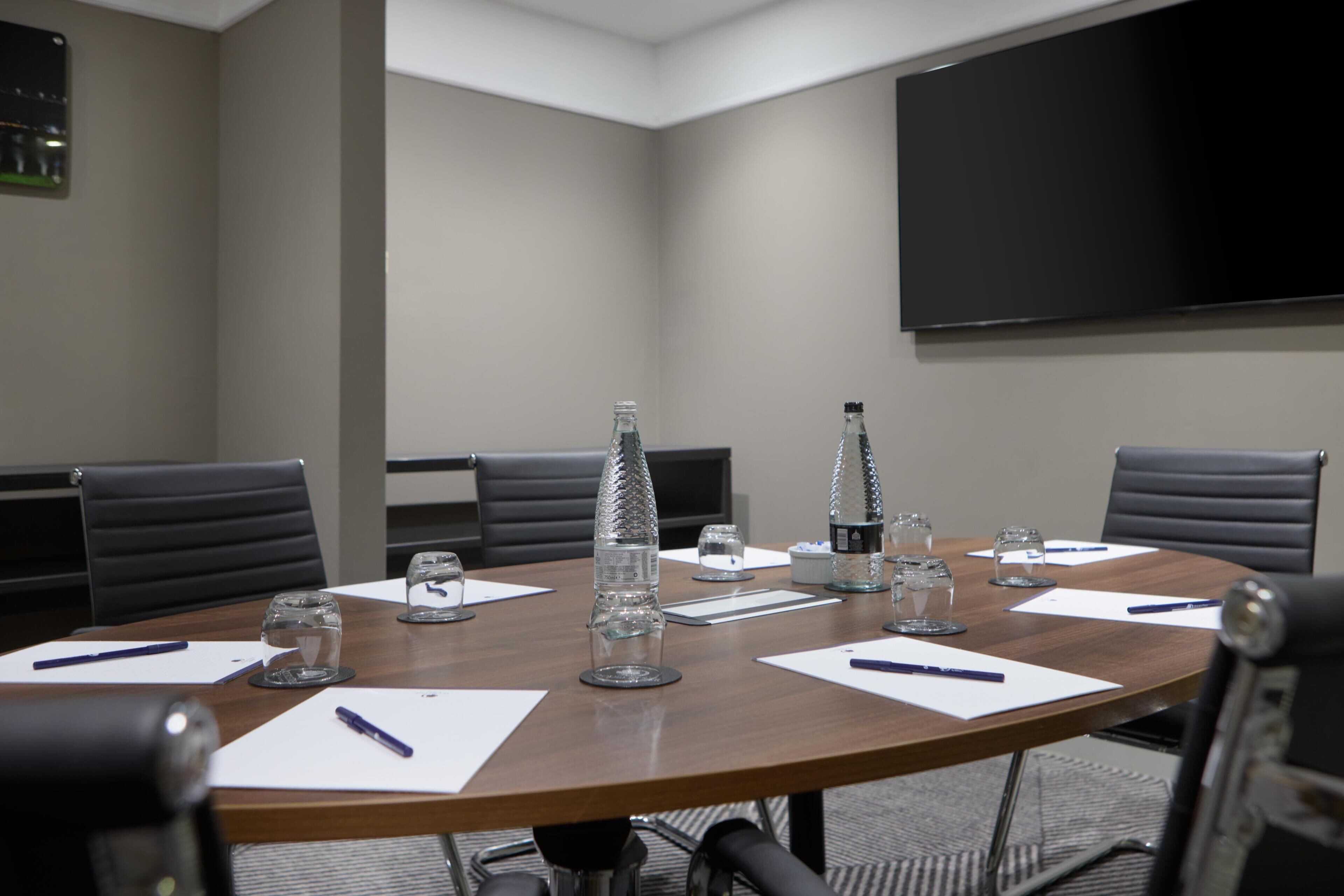 A conference room with a round table, chairs, a projector screen, and a television.