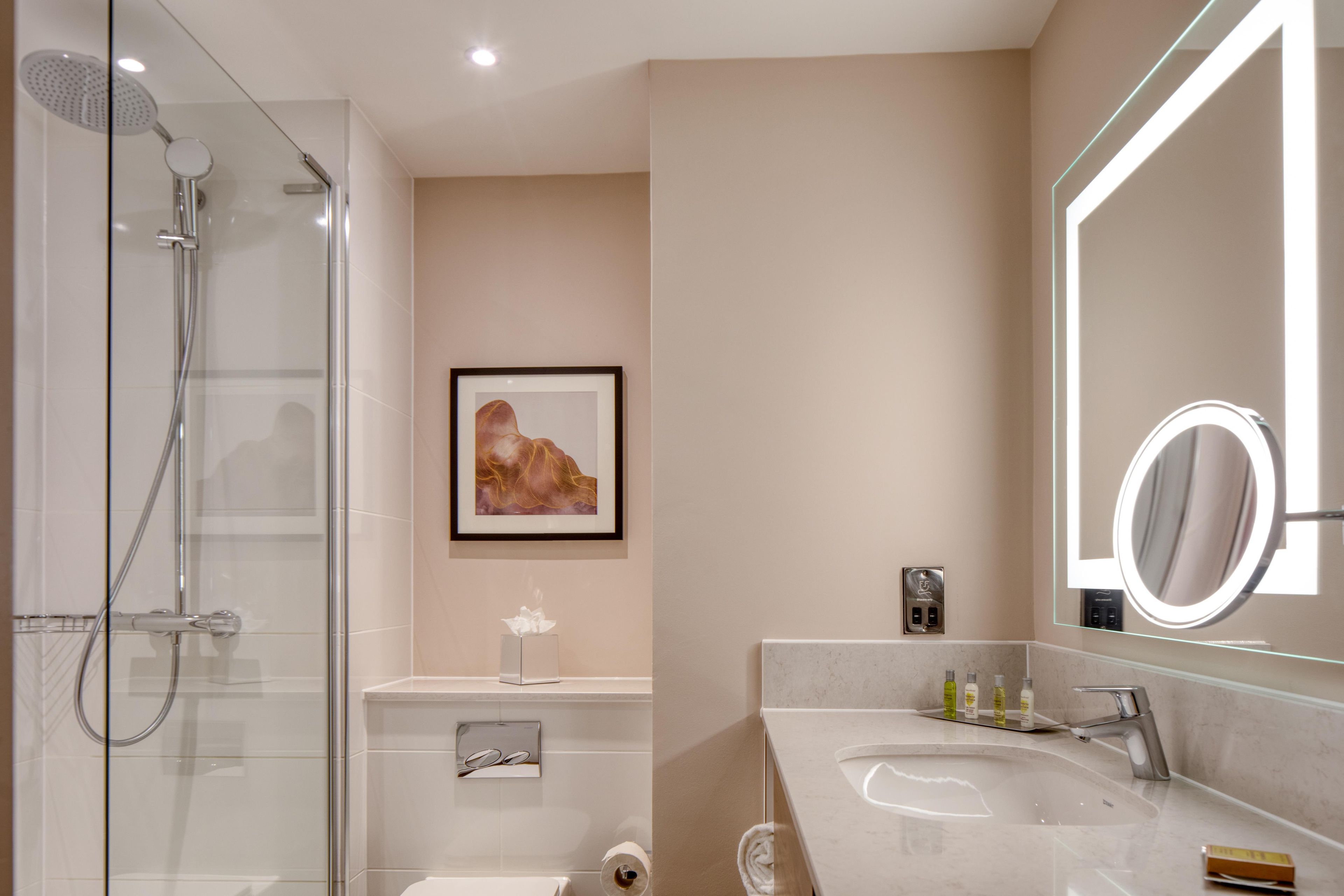 Un baño moderno con cabina de ducha acristalada, un espejo grande y un lavabo de mármol.