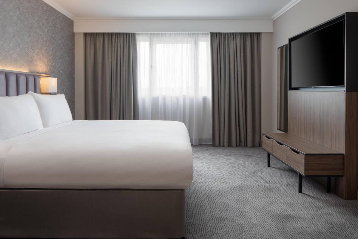Een hotelkamer met een groot bed, een televisie, een bureau en een raam met gordijnen.