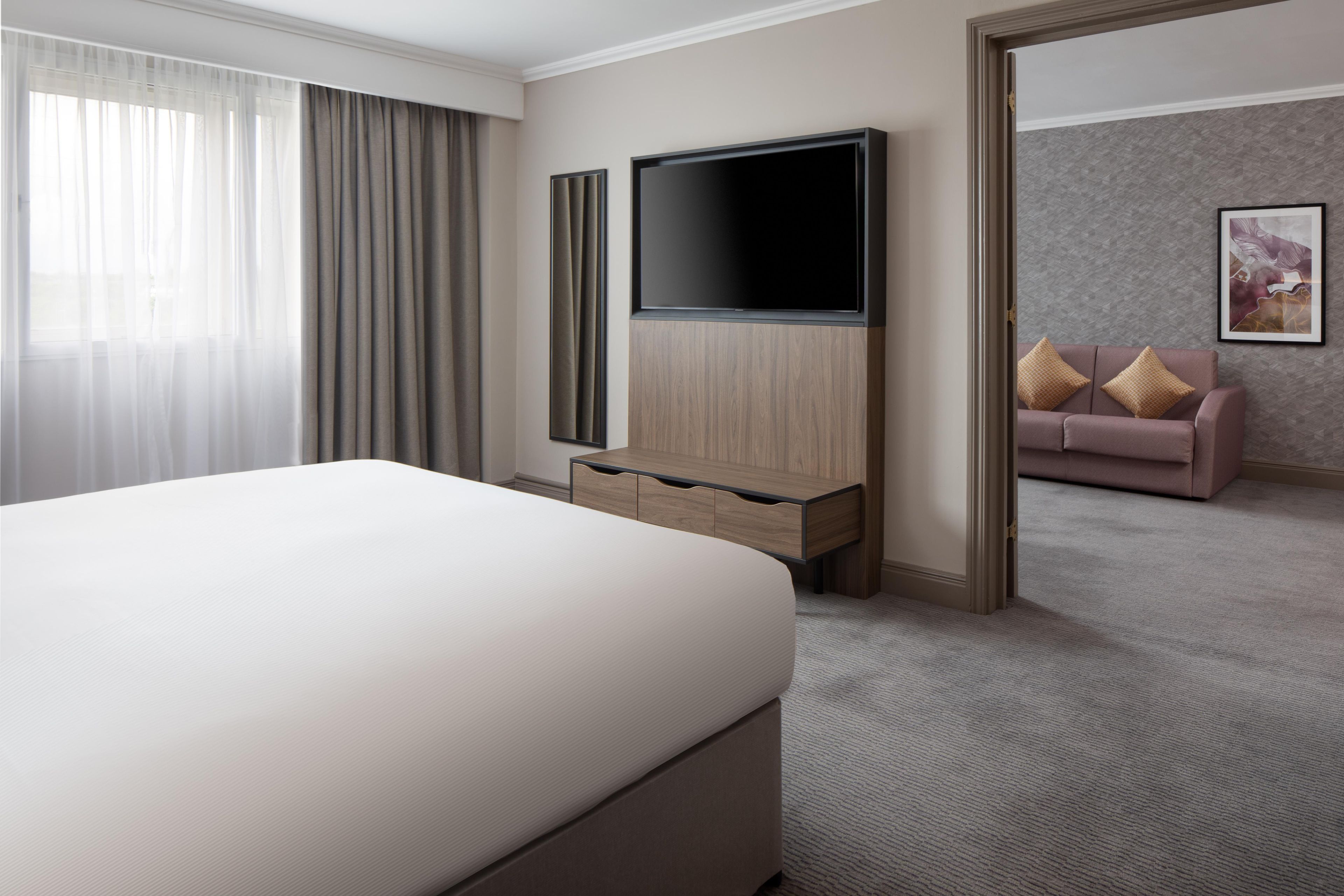 A hotel room with a bed, a TV, a dresser, a sofa, and a painting on the wall.