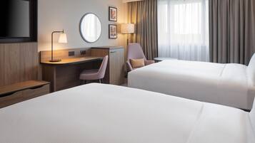 Habitación de hotel con dos camas, un escritorio, una silla, un televisor y un ventanal con cortinas.