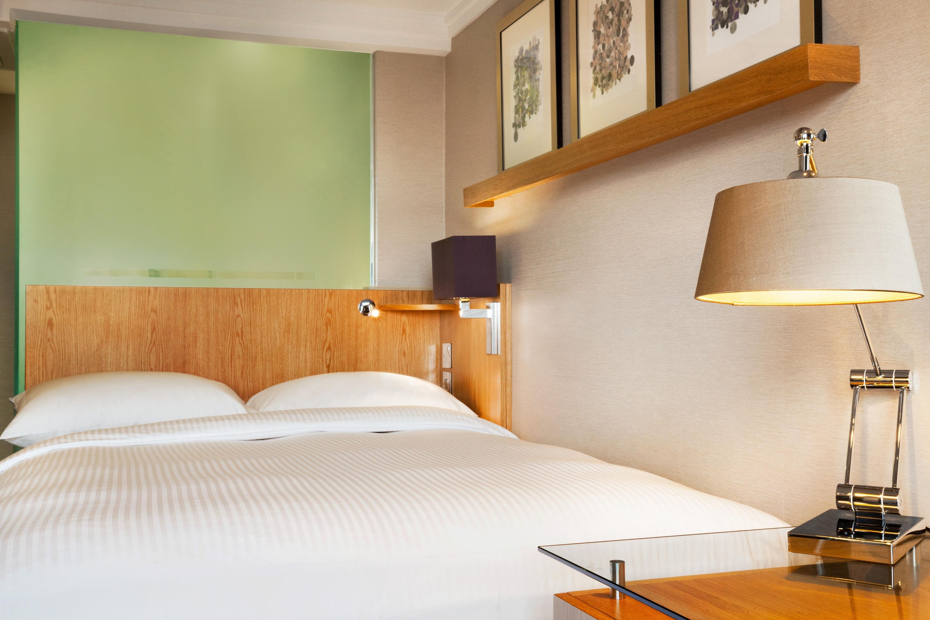 Una habitación de hotel con una cama, una mesita de noche, una lámpara y una estantería con marcos.