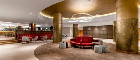 A spacious lobby with a central seating area, large pillars, and a modern ceiling design.