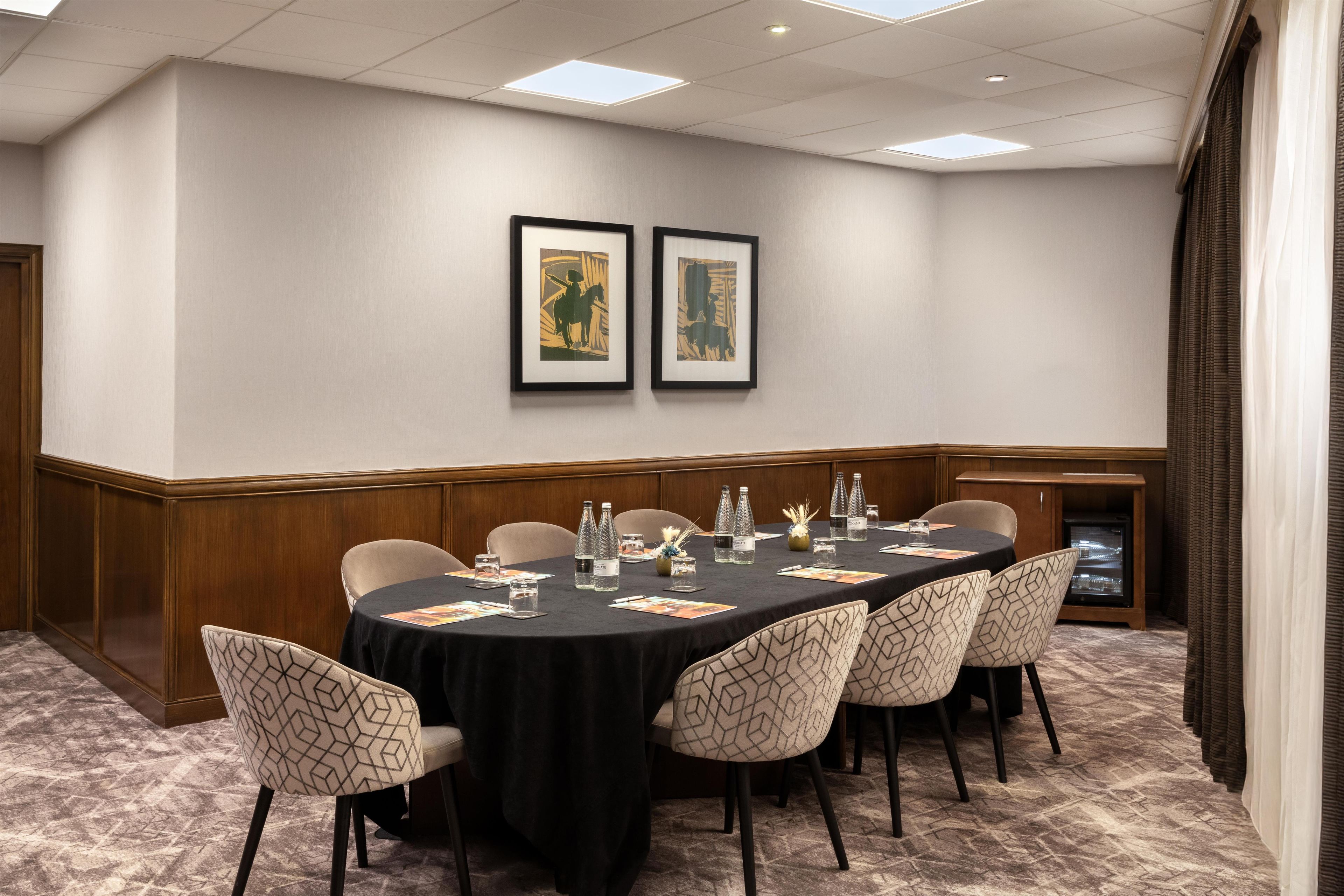 A conference room with a long table, chairs, framed artwork on the wall, and a water dispenser.