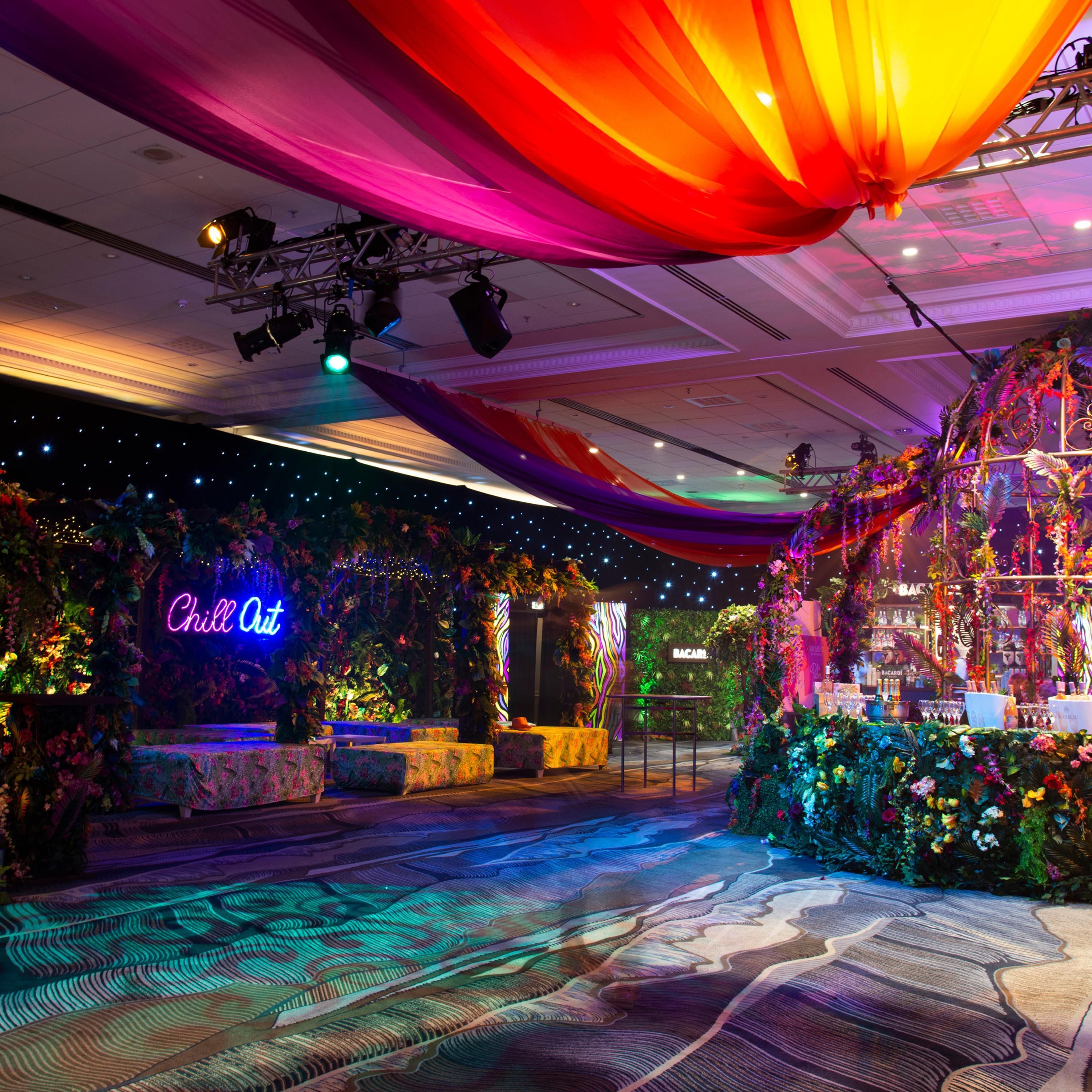 A stage with a 'Chill Out' neon sign, surrounded by lush greenery and floral arrangements.