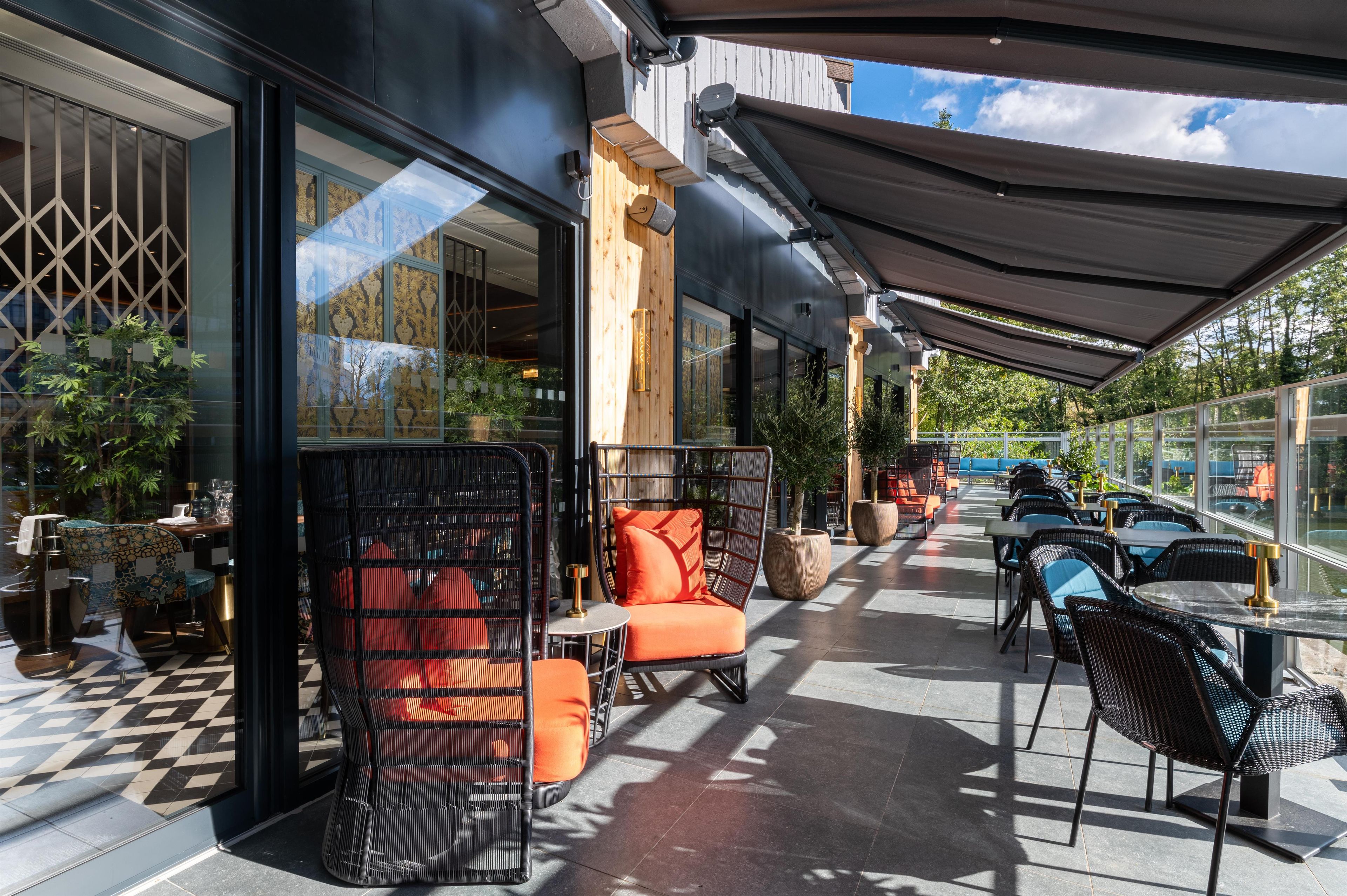 An outdoor seating area with wicker chairs and tables, a covered section with a large awning, and a view of the sky through the windows.