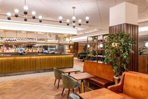 A bar area with a counter, seating, and a large potted plant. - Hilton Birmingham Metropole (Birmingham)