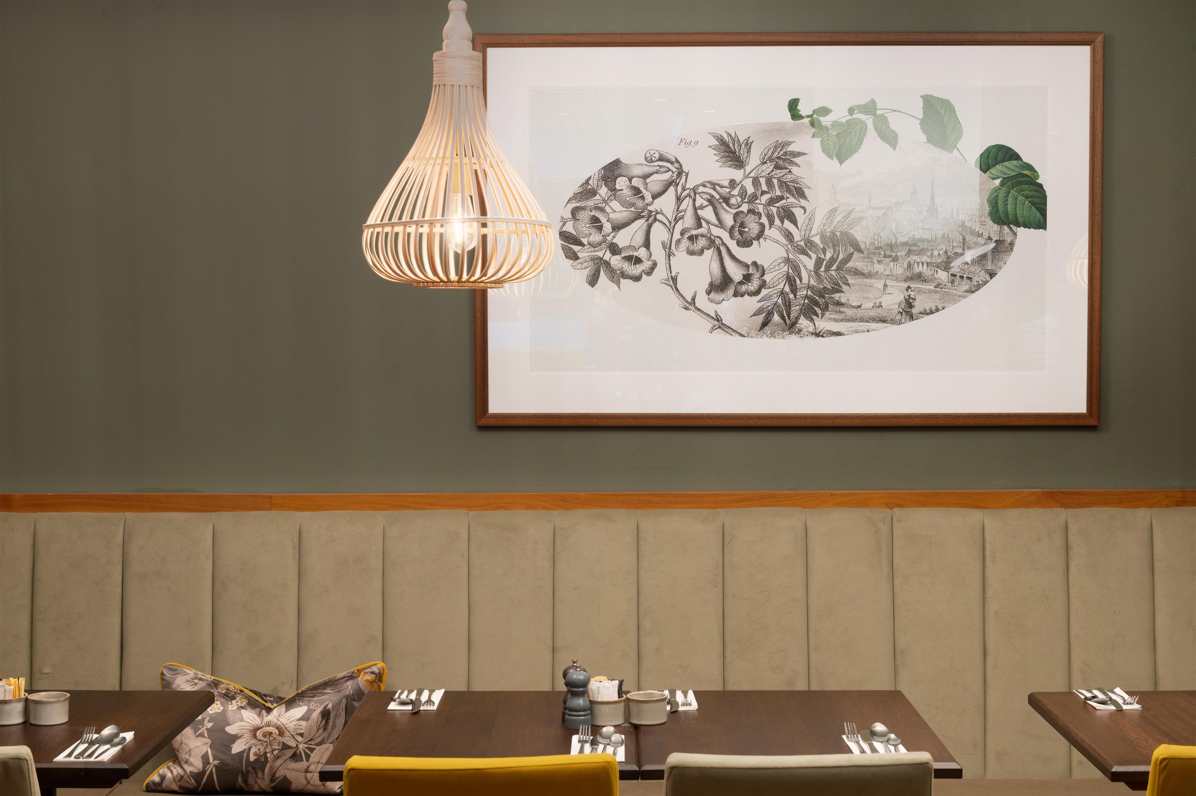 A dining area with a table set for two, a hanging light fixture, and a framed botanical illustration on the wall.