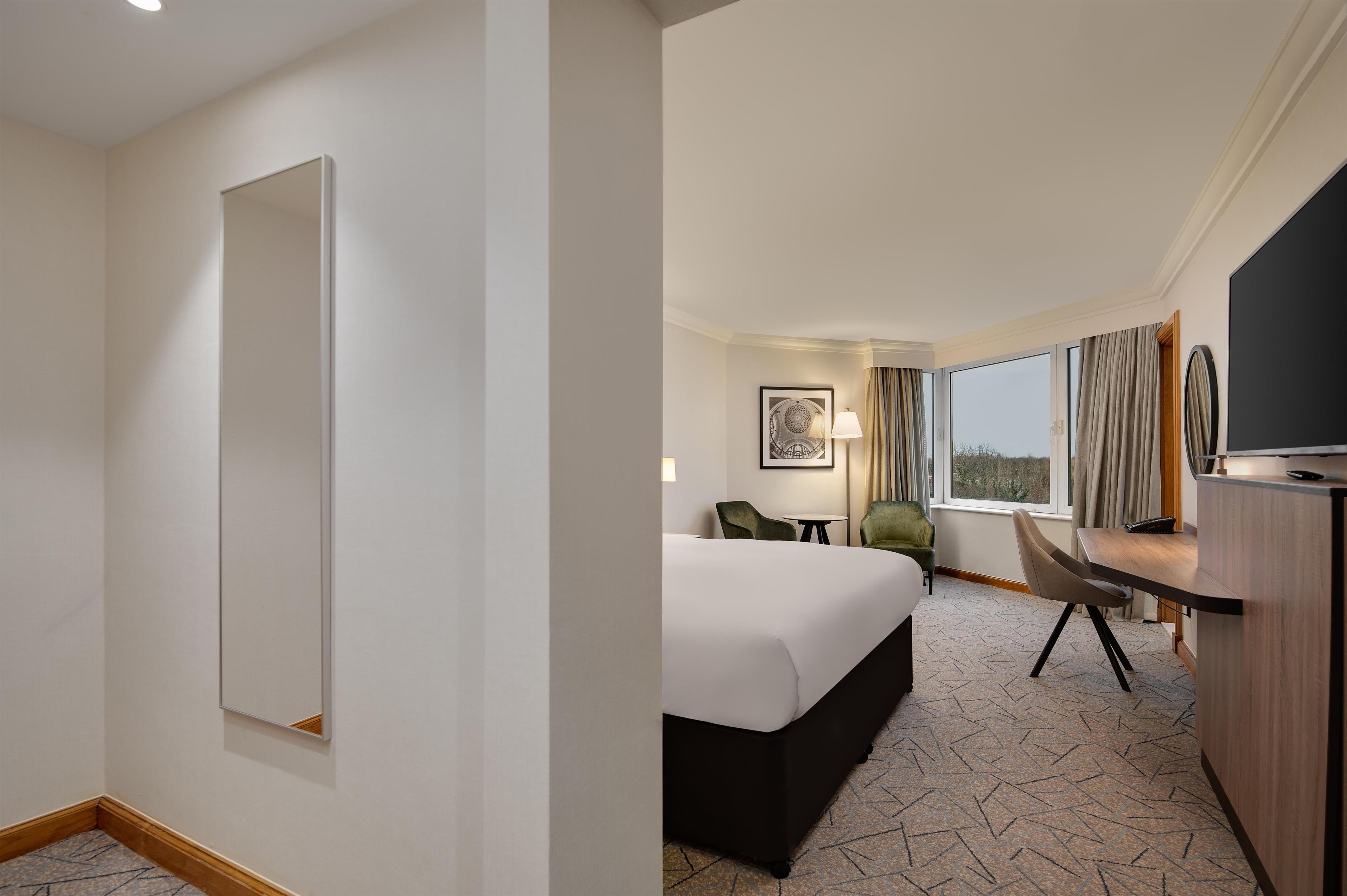 Una habitación de hotel con una cama grande, un escritorio, una silla, un televisor y una ventana con cortinas.