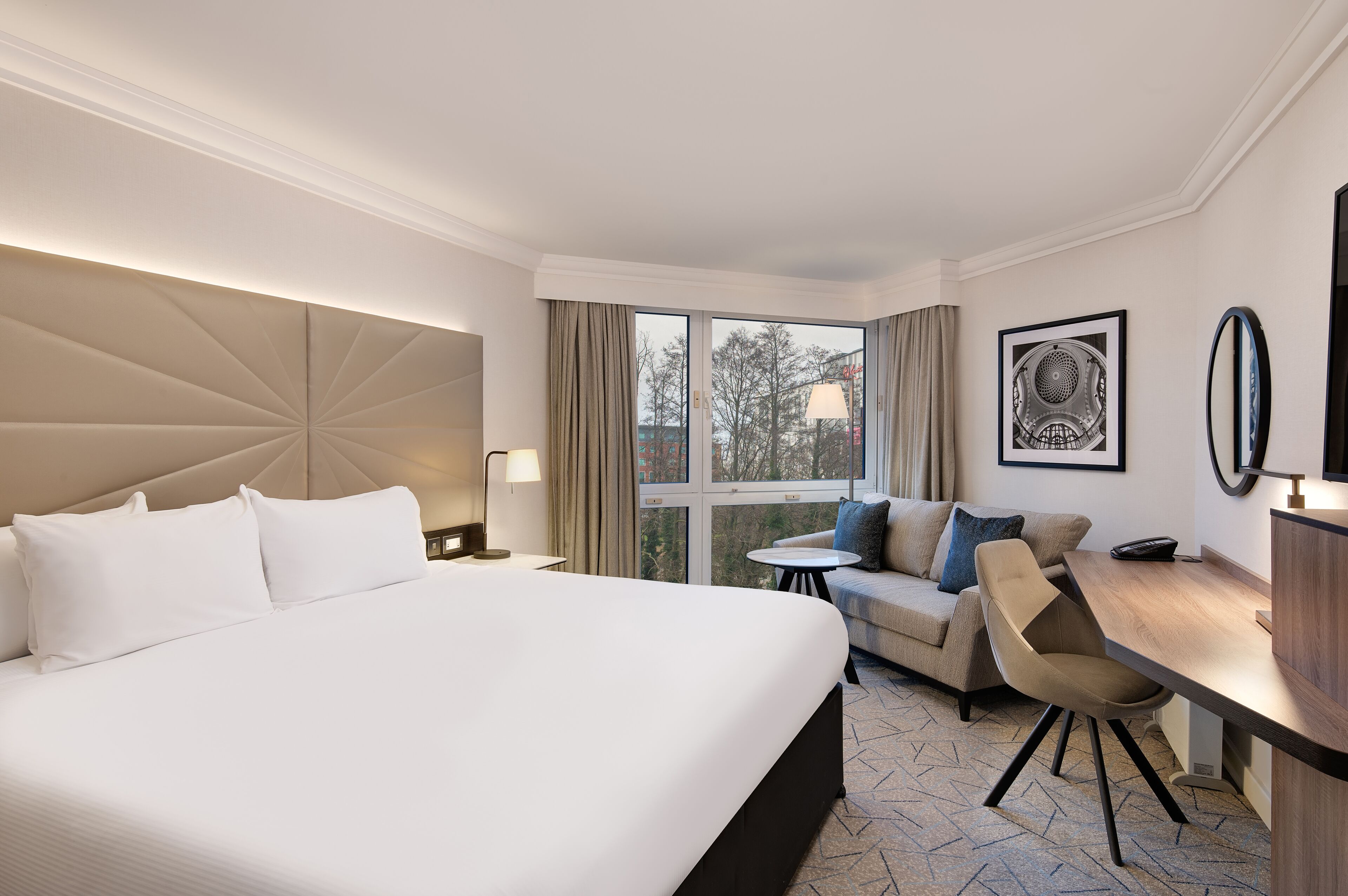 A hotel room with a large bed, a sofa, a small table, and a desk.