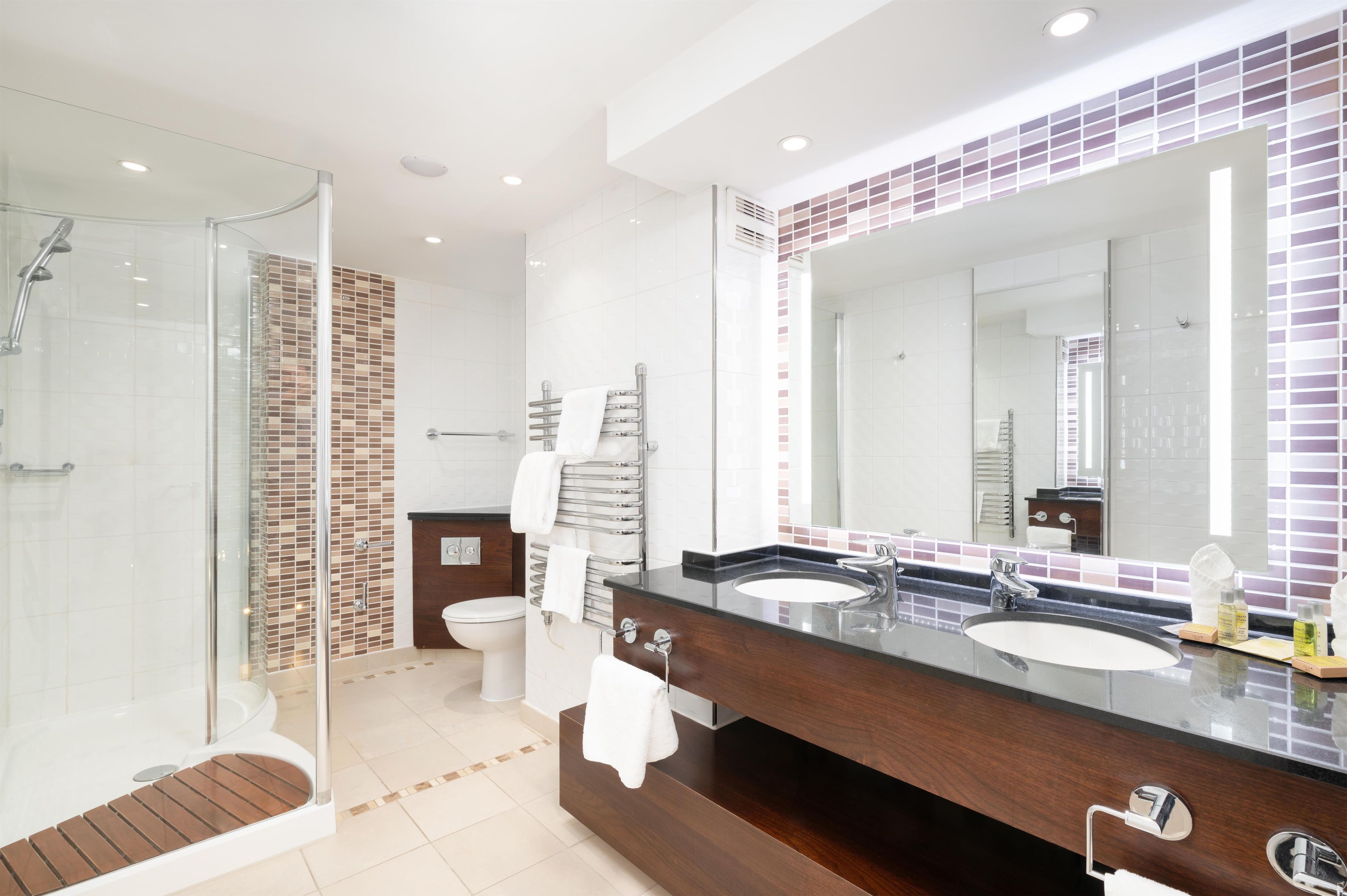 A modern bathroom with a glass shower enclosure, a vanity with two sinks, and a large mirror.