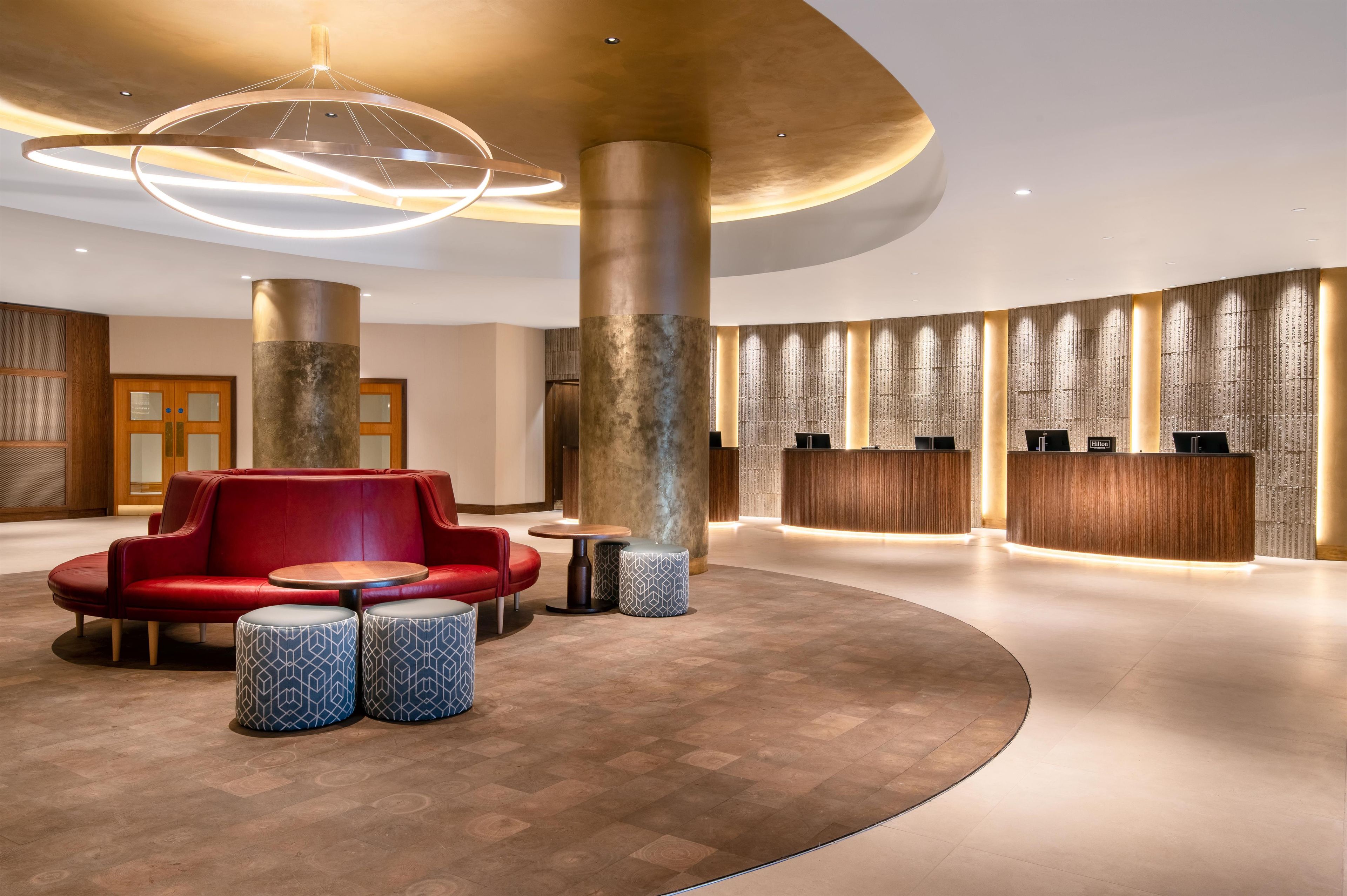 Un hall de hotel con un sofá rojo, mesas redondas y una recepción.