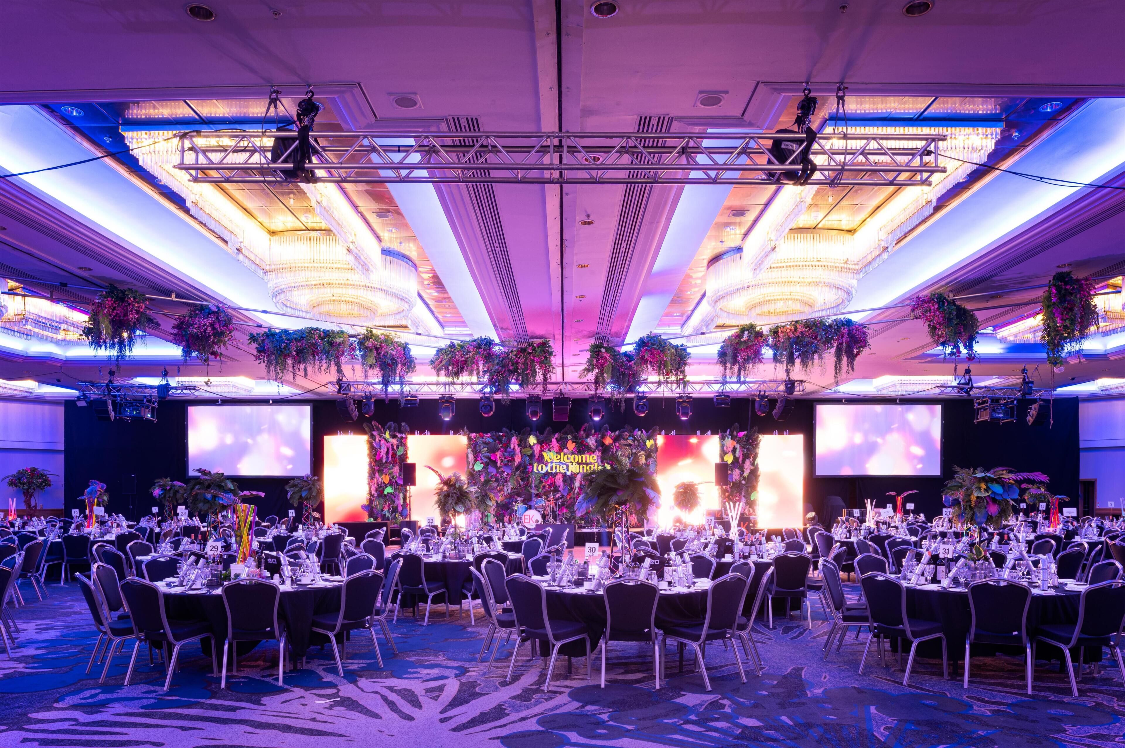 A banquet hall with round tables, chandeliers, and floral decorations.