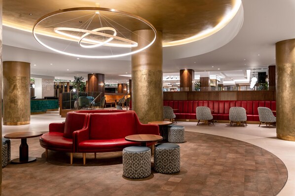 A modern lobby with a red seating area, wooden columns, and a unique circular light fixture.