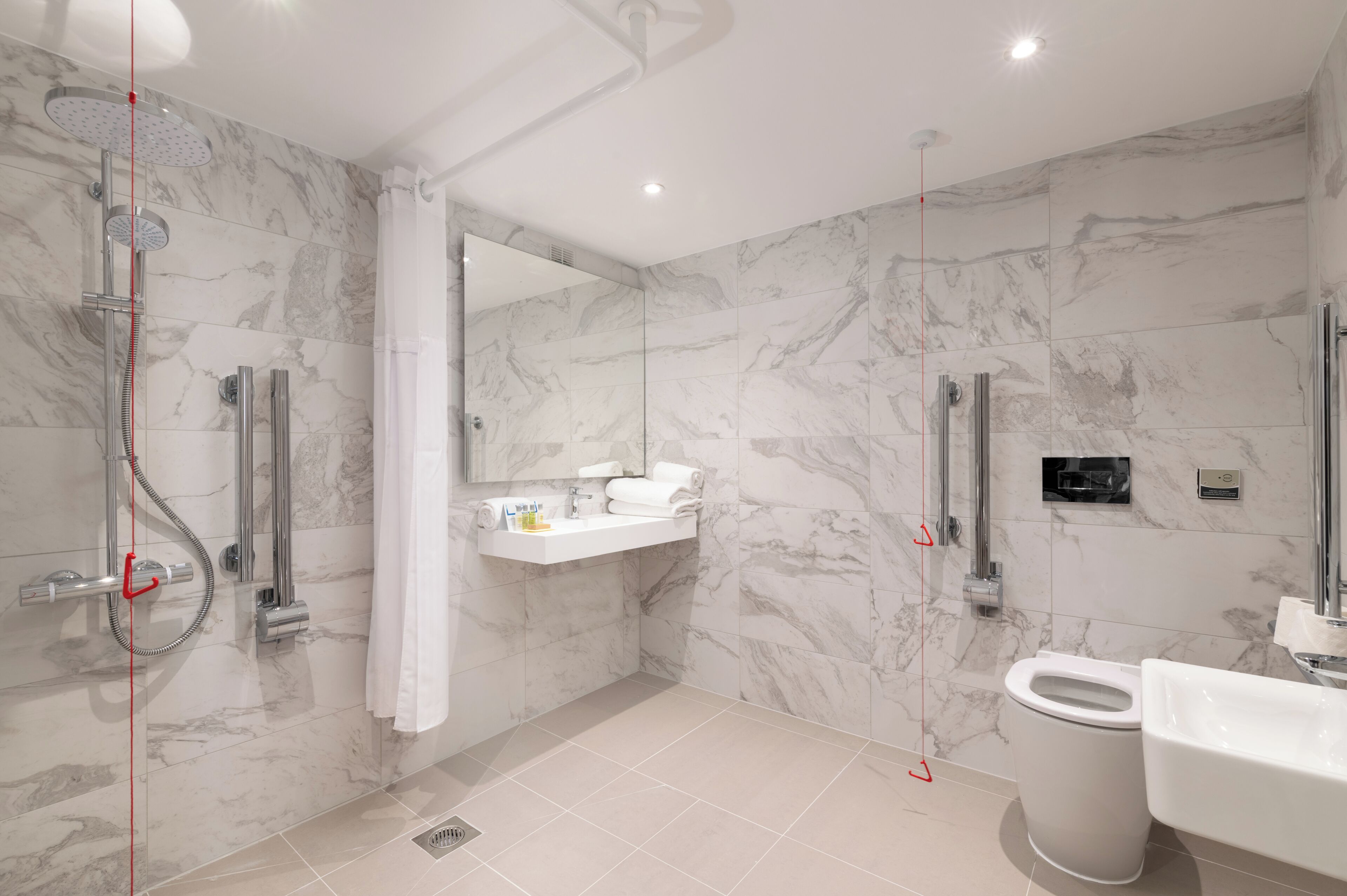 A modern bathroom with a shower, toilet, sink, and marble walls.