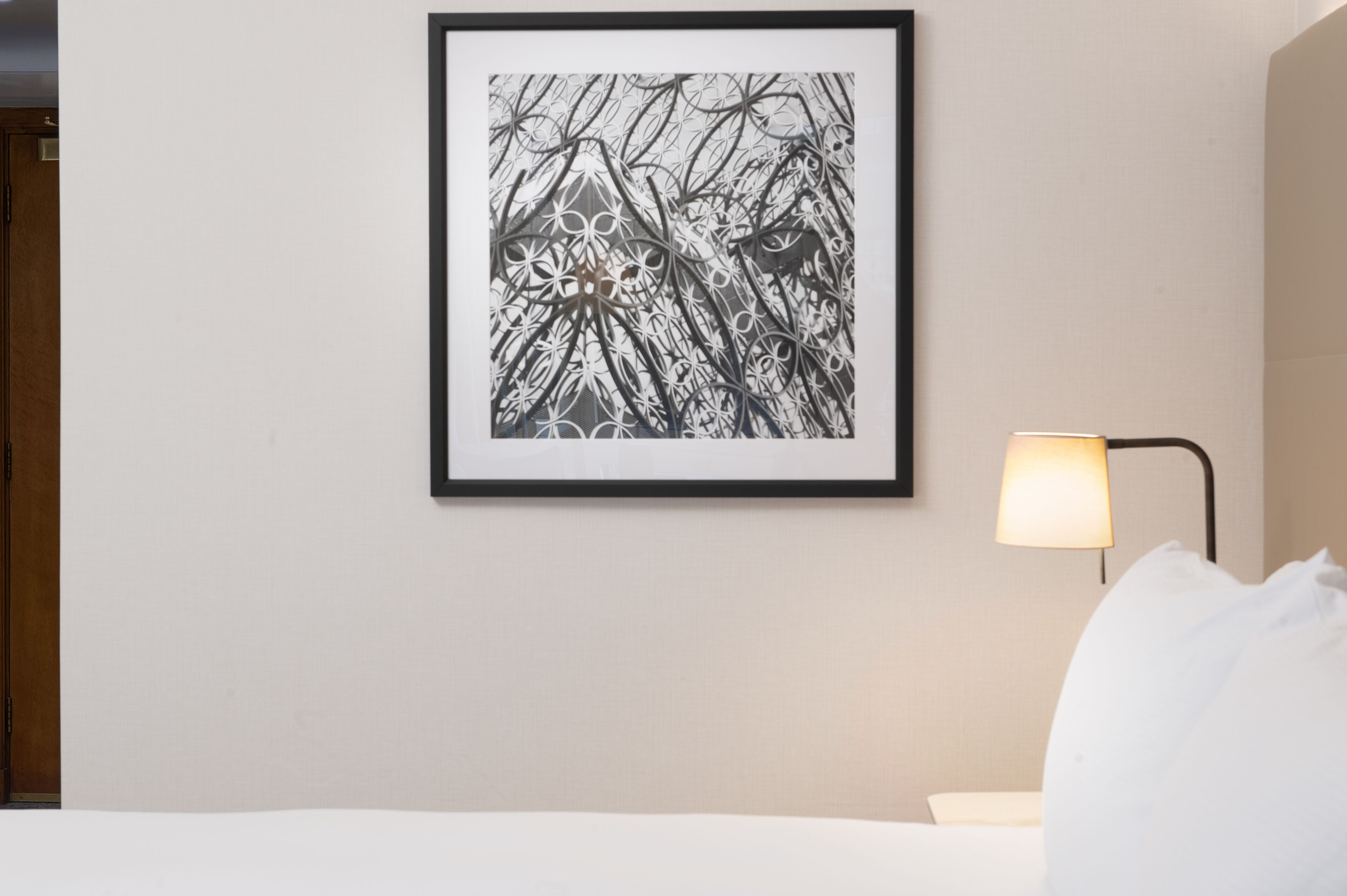 A framed abstract artwork on a wall, a bedside lamp, and a white bed with a pillow.