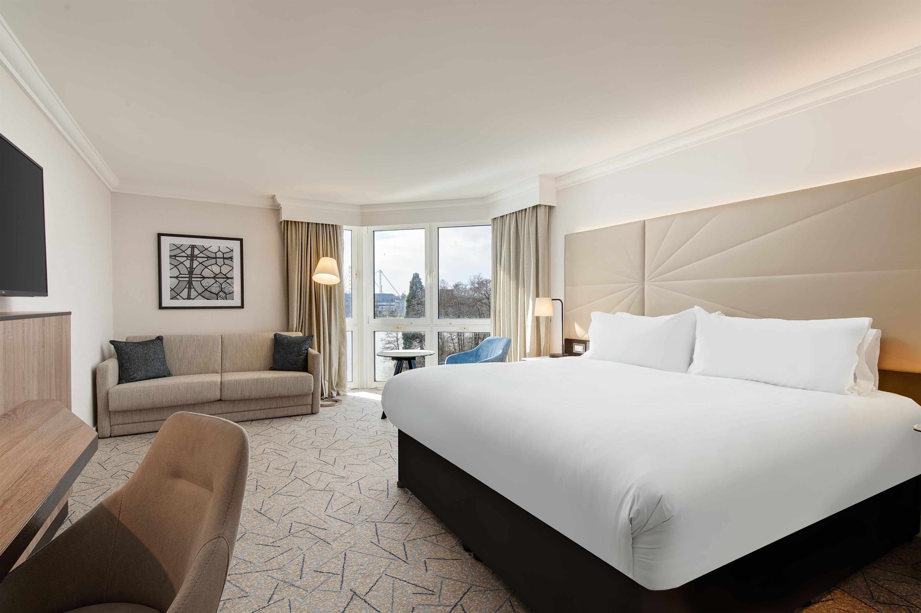 A hotel room with a large bed, a sofa, a desk, and a TV.
