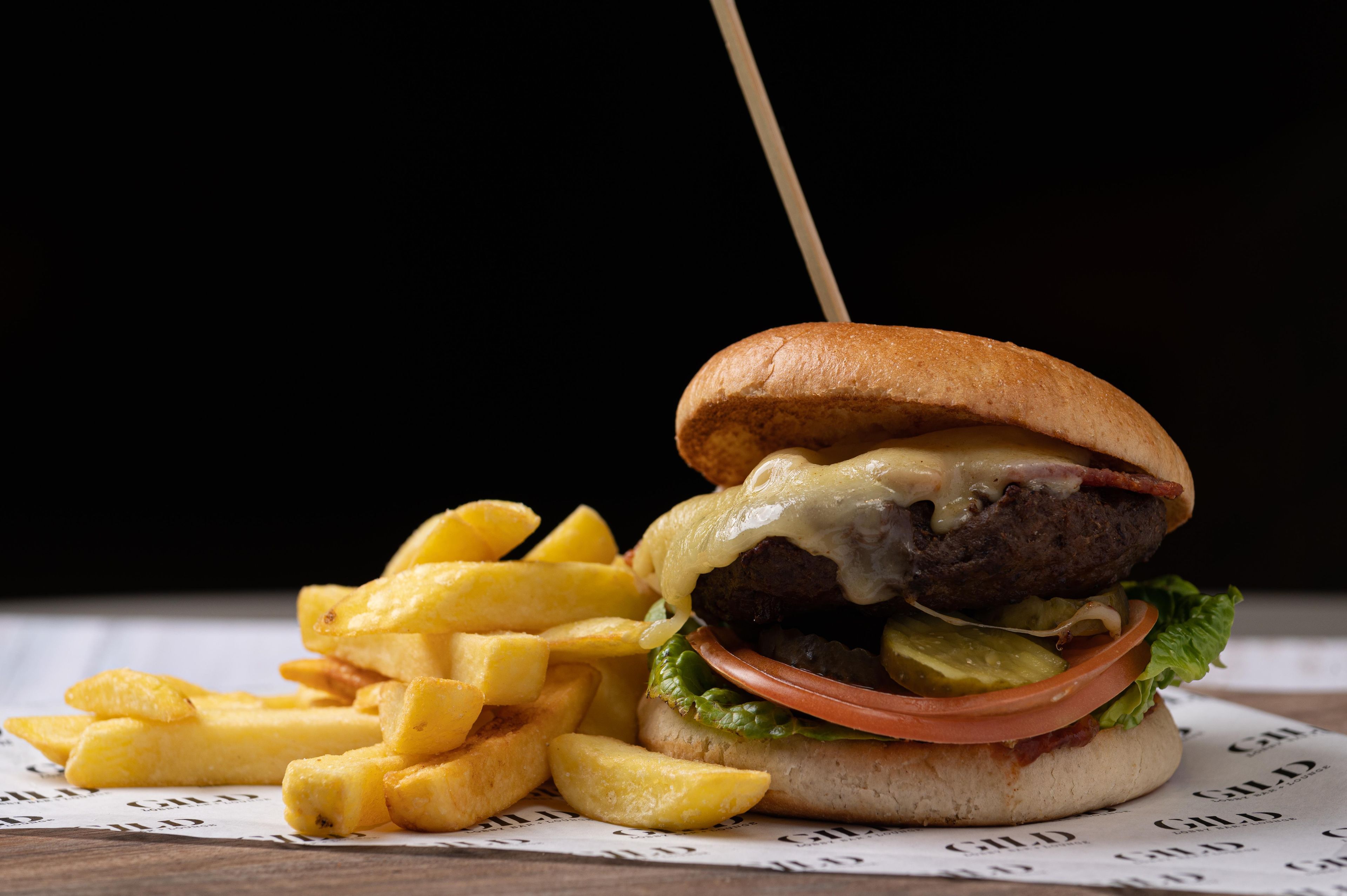 A burger with a bun, lettuce, tomato, and cheese, accompanied by French fries on a piece of paper with text.