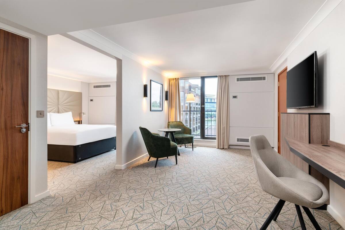 A hotel room with a bed, a desk, a chair, a TV, and a window with curtains.