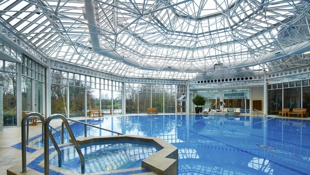 Piscina interior con techo de cristal, rodeada de zonas de estar y vistas a árboles.