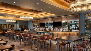 A bar area with multiple seating options, a bar counter, and a variety of bottles and glasses. - Hilton Birmingham Metropole (Birmingham)