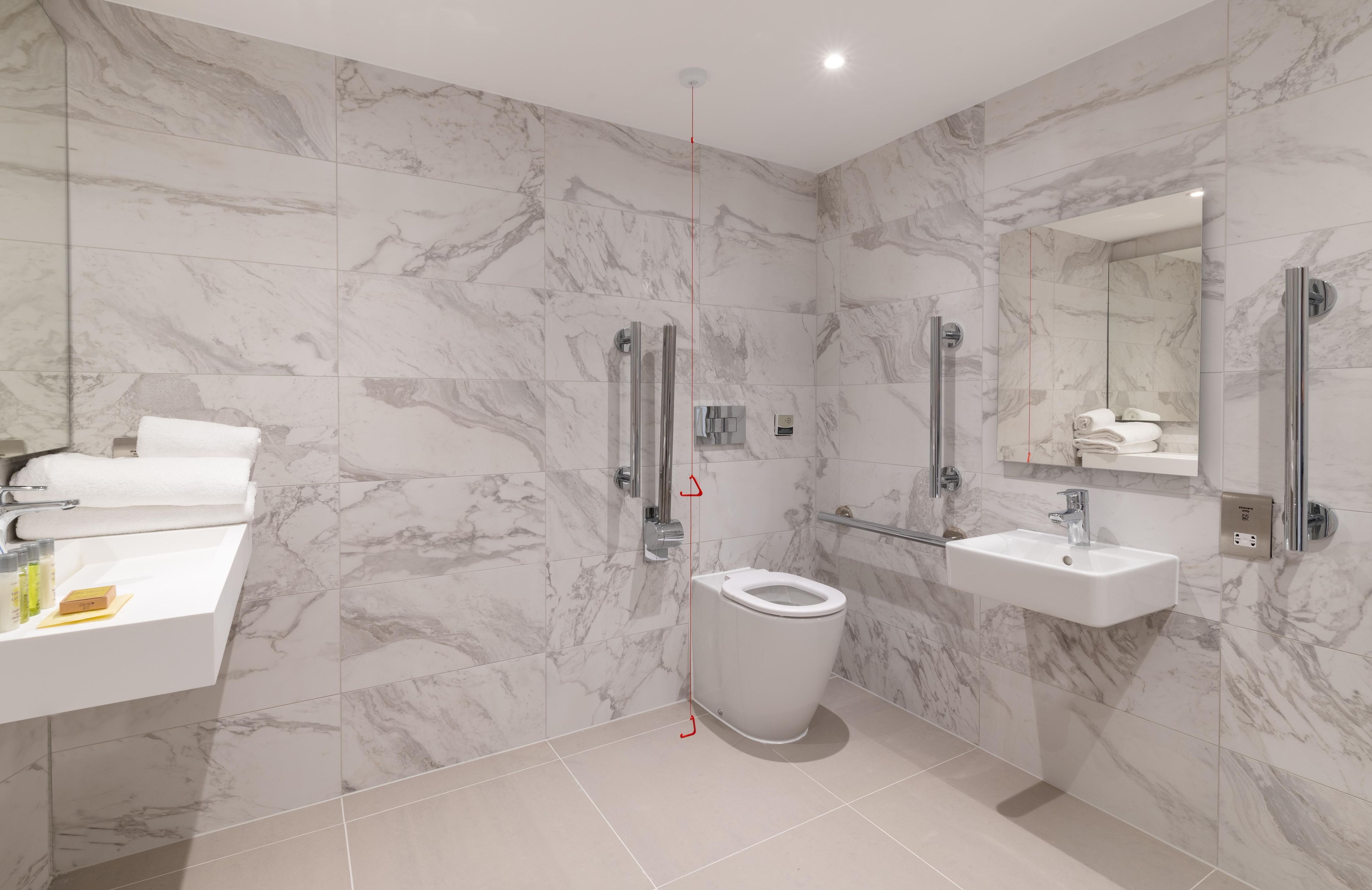 Un baño moderno con inodoro, lavamanos y zona de ducha, con azulejos de mármol y cerramiento de vidrio para la ducha.