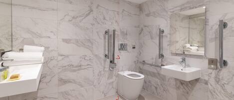 Un baño moderno con inodoro, lavamanos y zona de ducha, con azulejos de mármol y cerramiento de vidrio para la ducha.