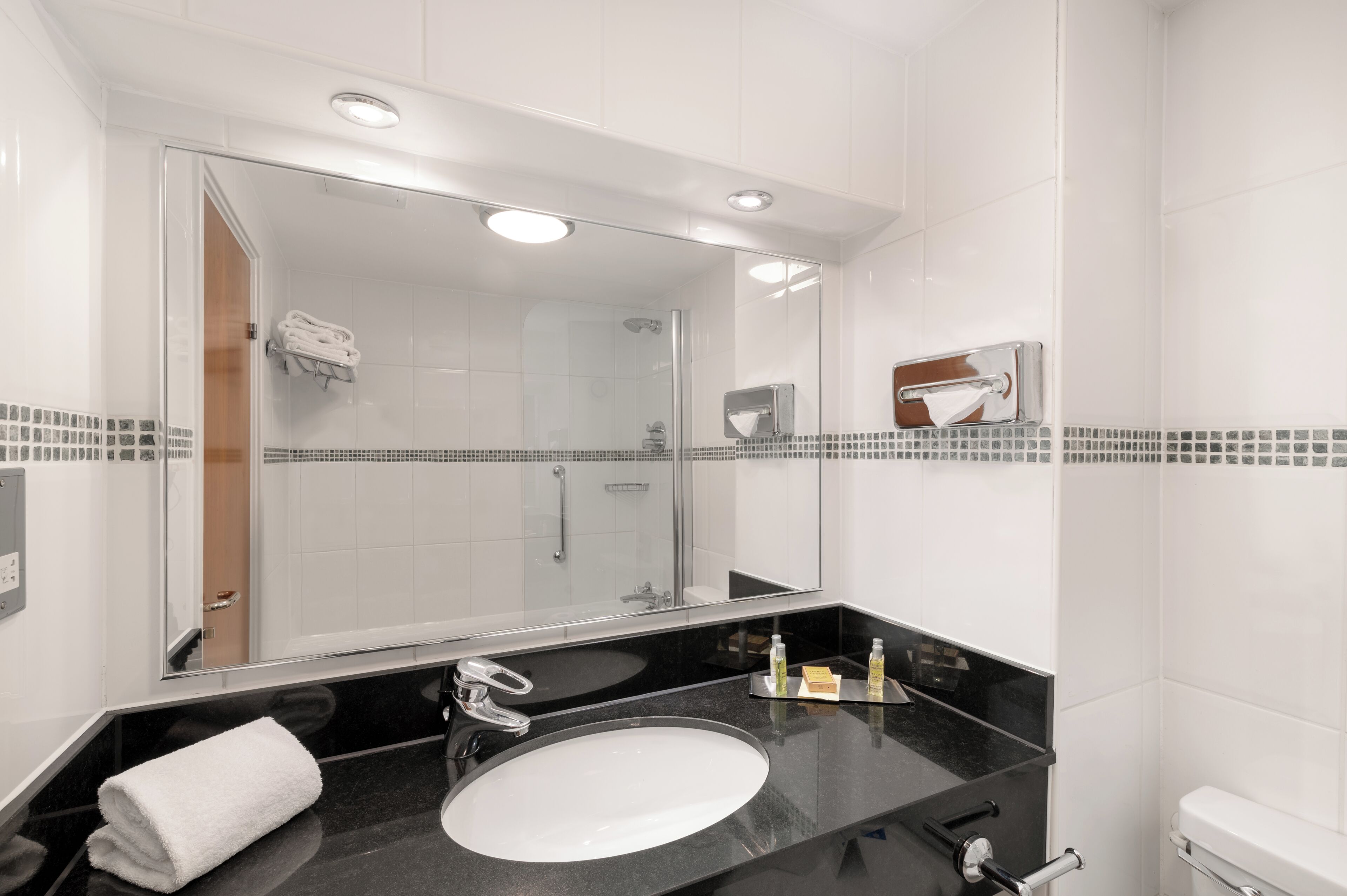 A modern bathroom with a large mirror, a black countertop, a white sink, and a glass-enclosed shower.