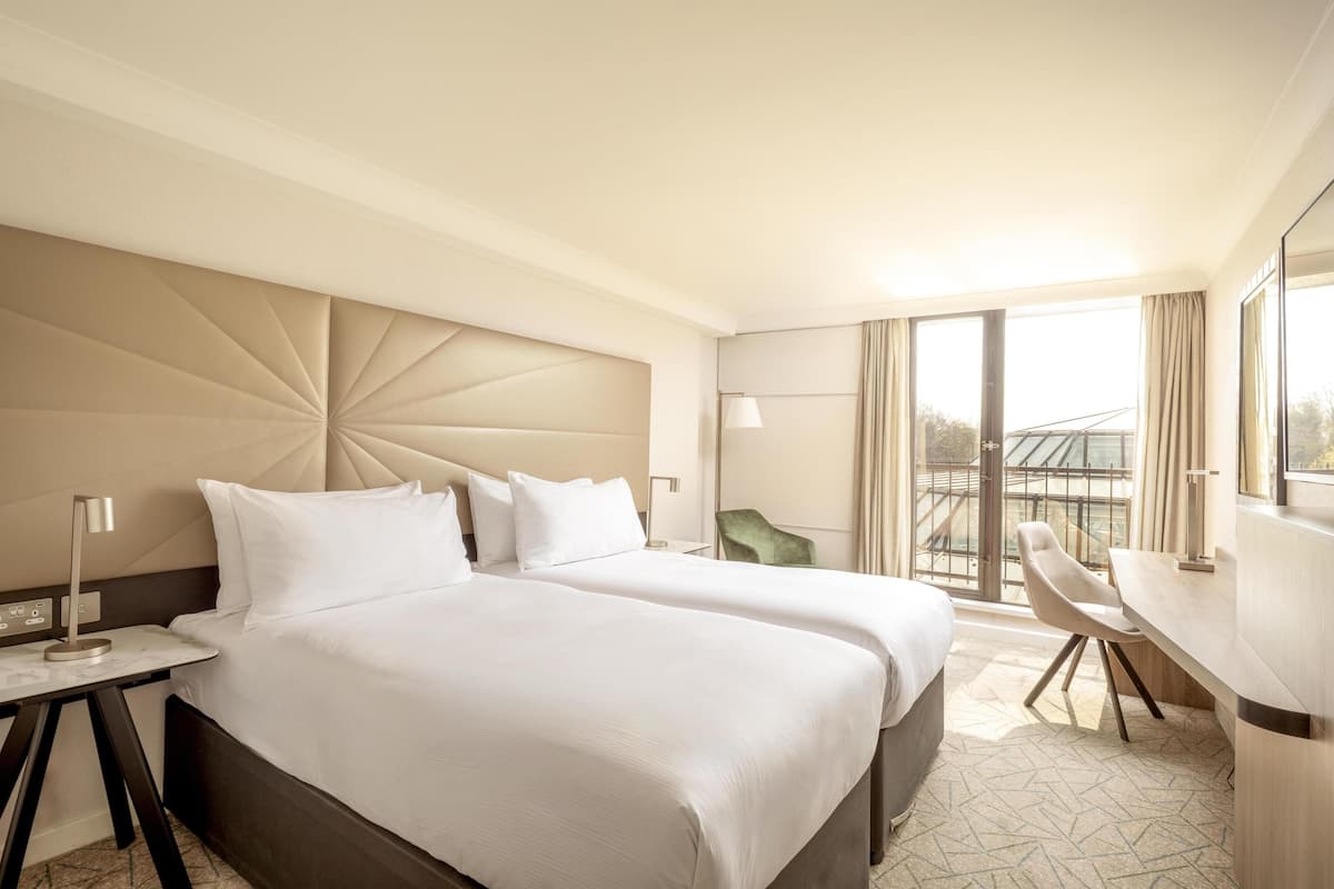 A hotel room with two beds, a desk, a chair, and a large window with a view.