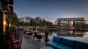 Una terraza en la azotea con mobiliario exterior, vistas a un edificio moderno y una masa de agua.