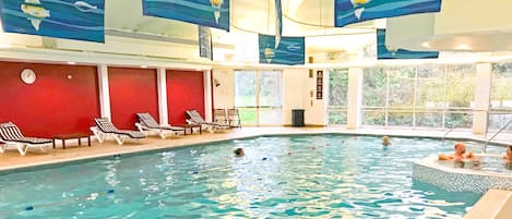 Une piscine intérieure dotée de chaises longues et d’une horloge au mur.