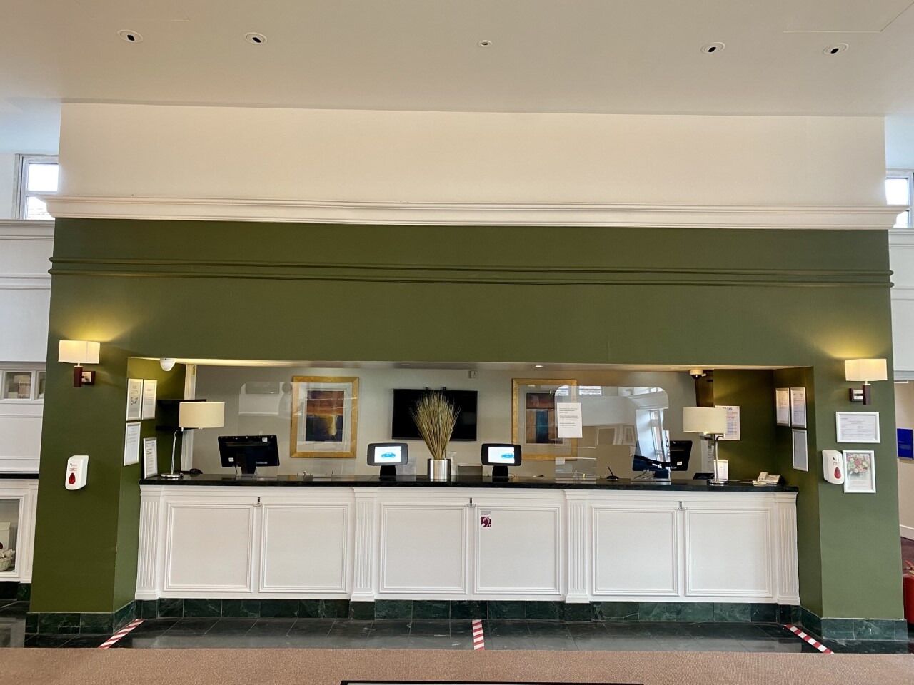 A reception desk with a green wall, white cabinets, and a marble floor.