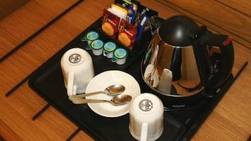 A tray with a coffee maker, two mugs, a plate with a spoon, and packets of milk and cookies.