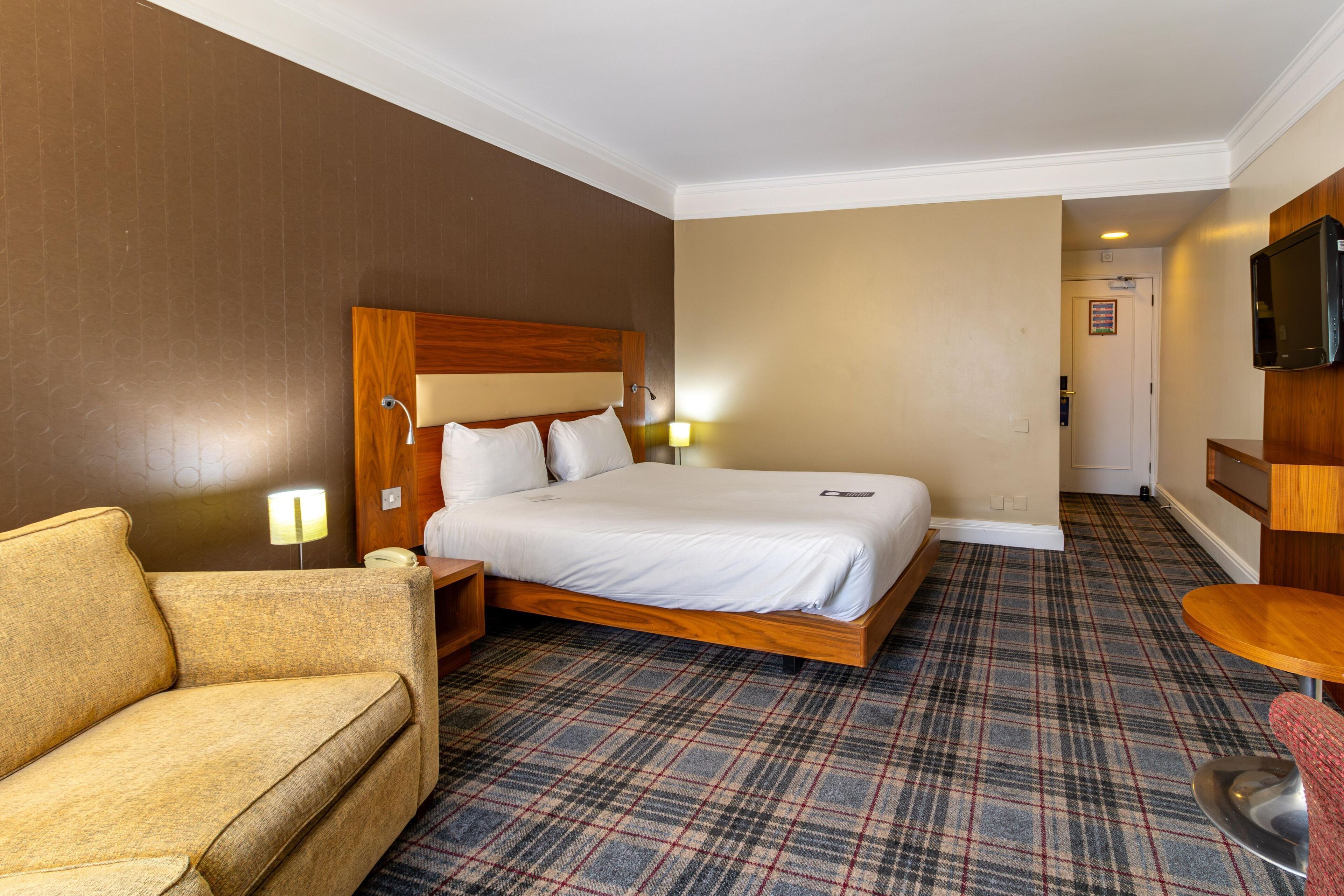 A hotel room with a large bed, a sofa, a TV, and a small table.