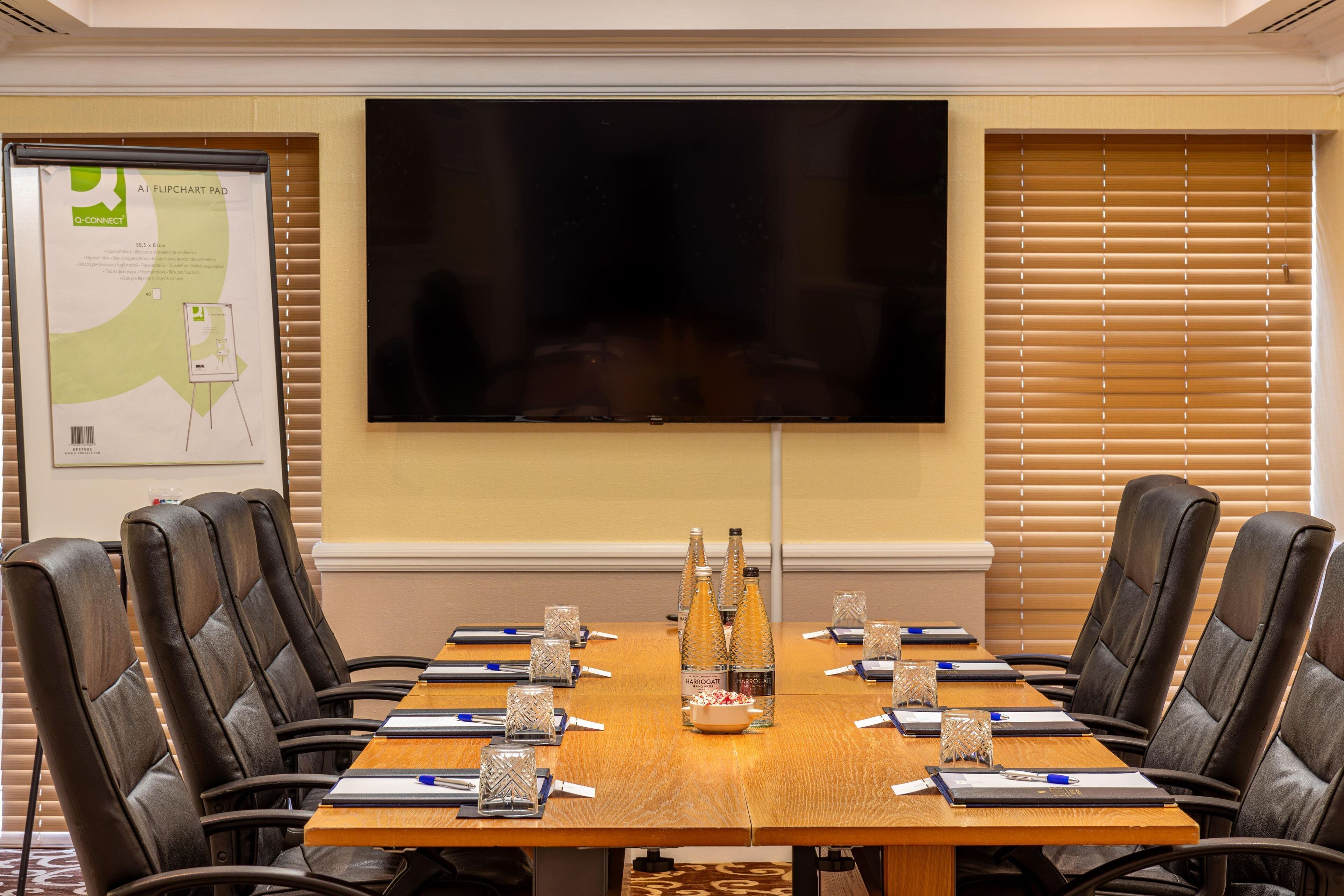 A conference room with a large flat-screen TV, a flip chart, and a table set for a meeting.