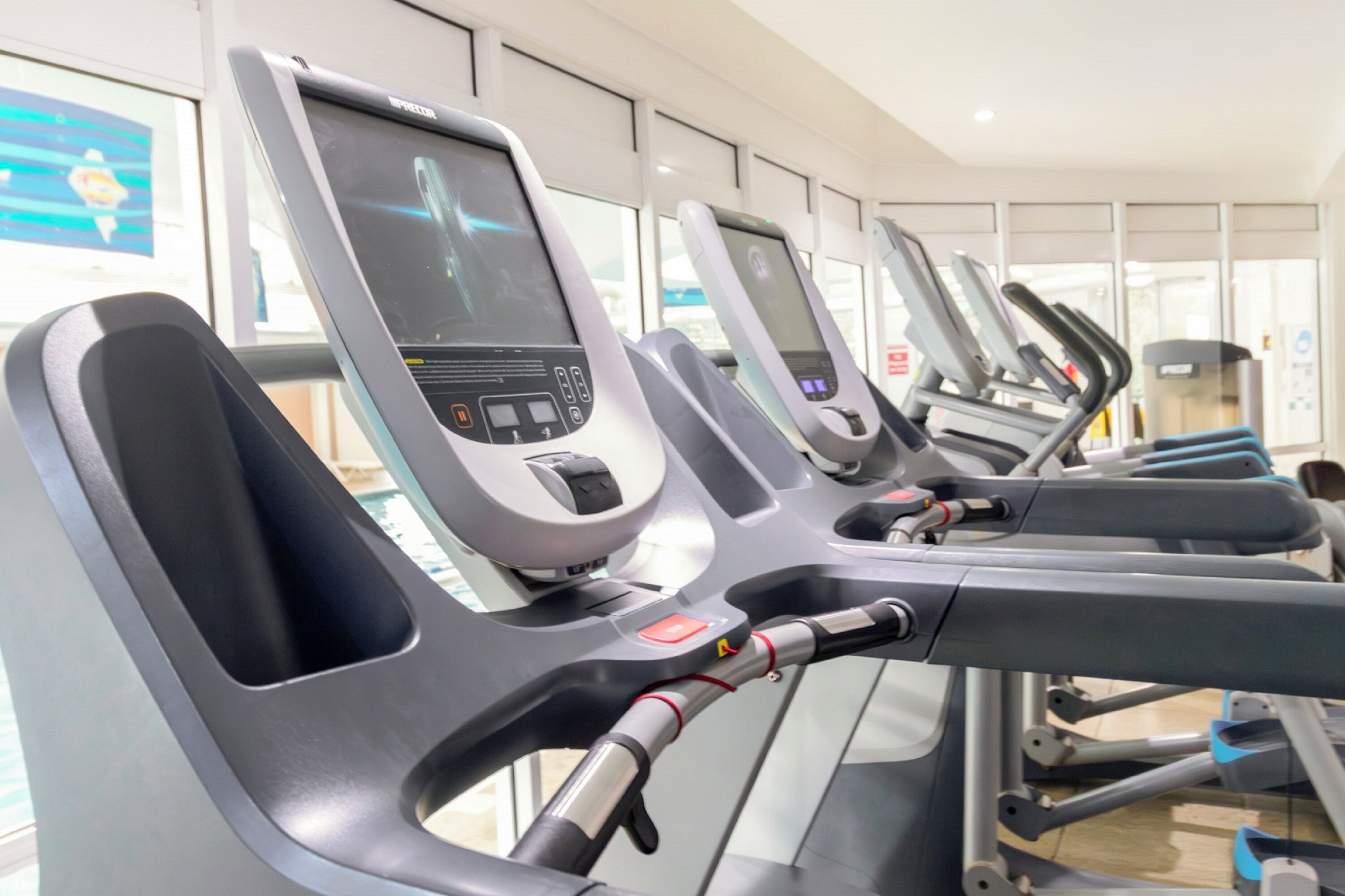 A row of stationary exercise bikes with digital displays and control panels, in a well-lit indoor setting.