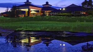 A large building with a central open pavilion and two smaller towers, surrounded by a grassy area and a body of water reflecting the structure. - Bromsgrove Hotel (Bromsgrove)