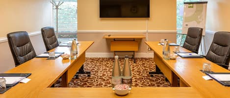 Una sala de conferencias con una mesa larga, cuatro sillas, una pantalla de televisión y piso alfombrado.