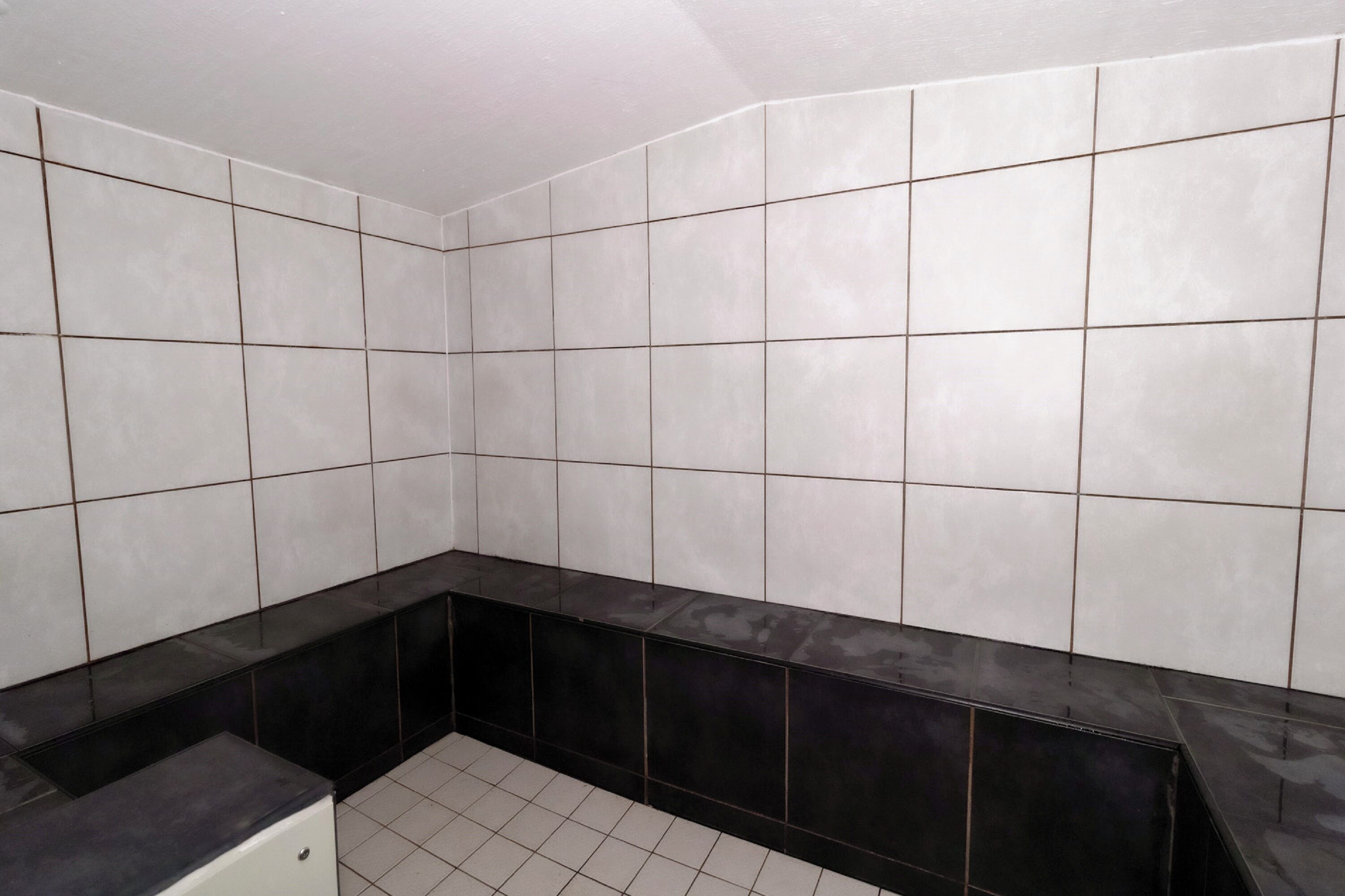 A bathroom with white tiled walls and a black countertop.