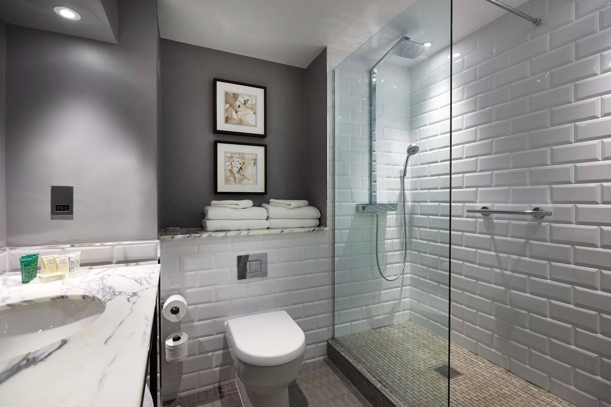 A modern bathroom with a glass-enclosed shower, marble sink, and a toilet.