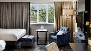 Une chambre d’hôtel avec un lit, un bureau, une chaise, une petite table et un téléviseur.
